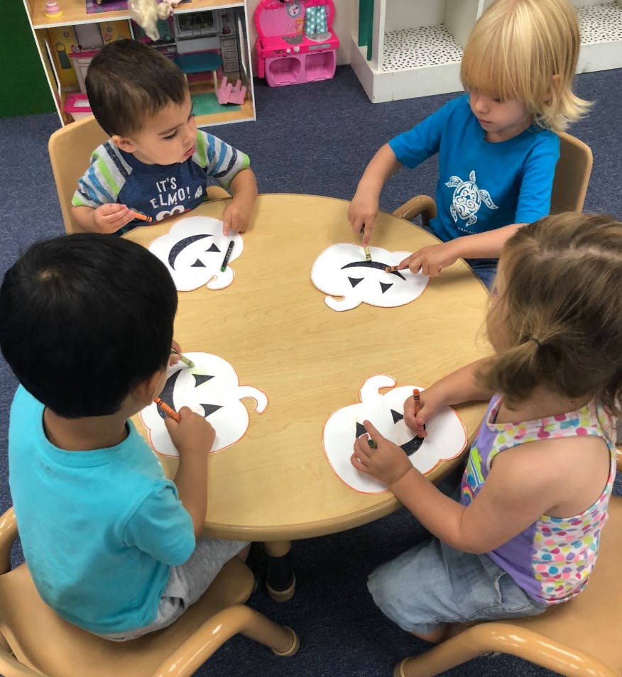 Four children sitting at a table making pumpkin crafts