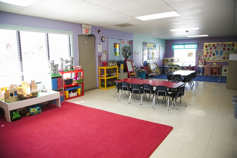 Classroom with small tables and chairs, a red rug, and toys