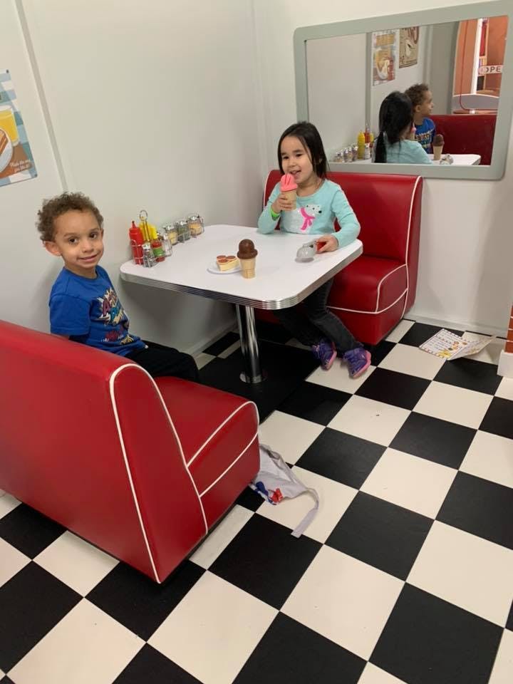 Two children sitting in a diner booth, one eating ice cream