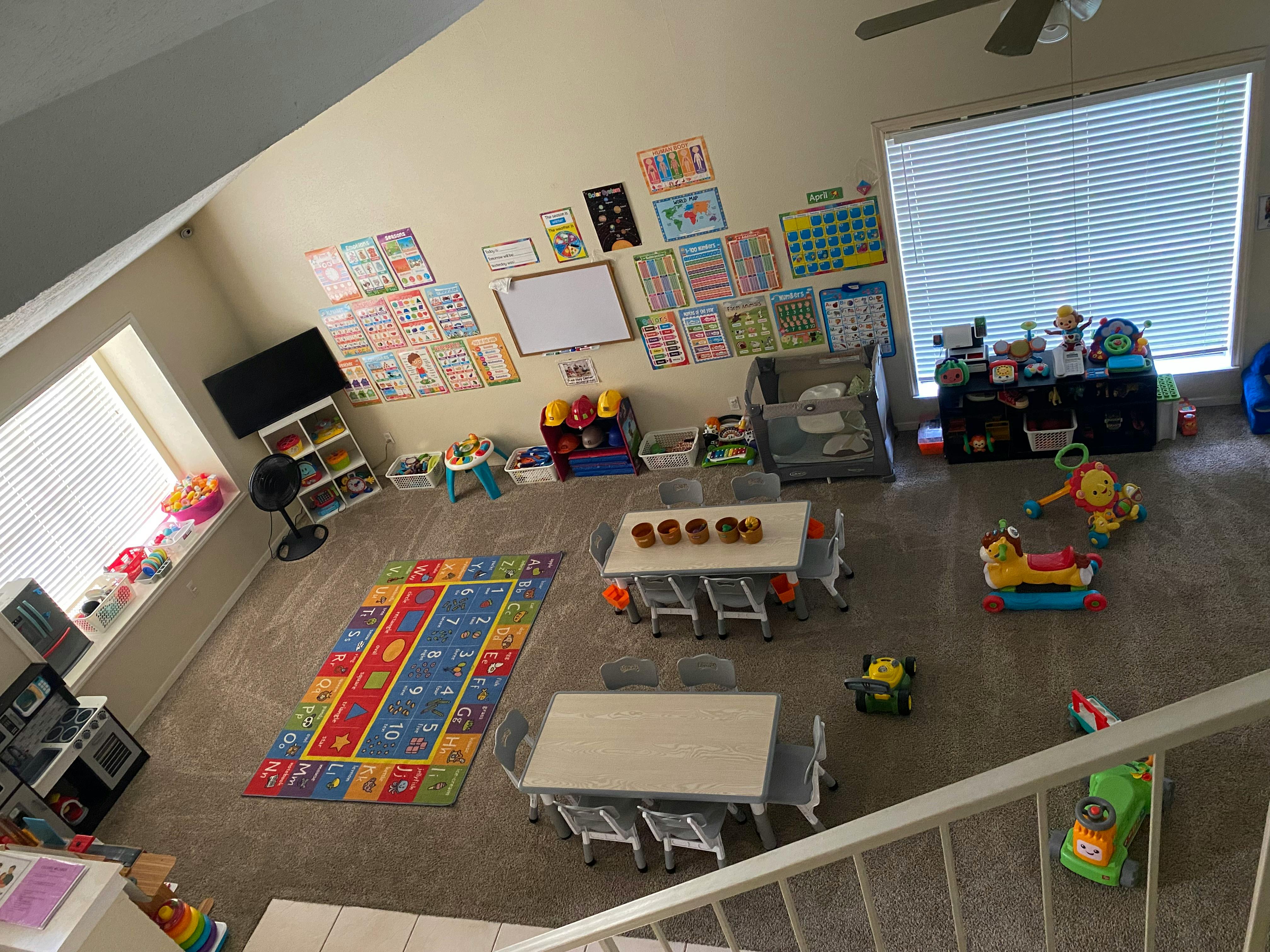Playroom with tables, chairs, toys, and educational posters on the wall