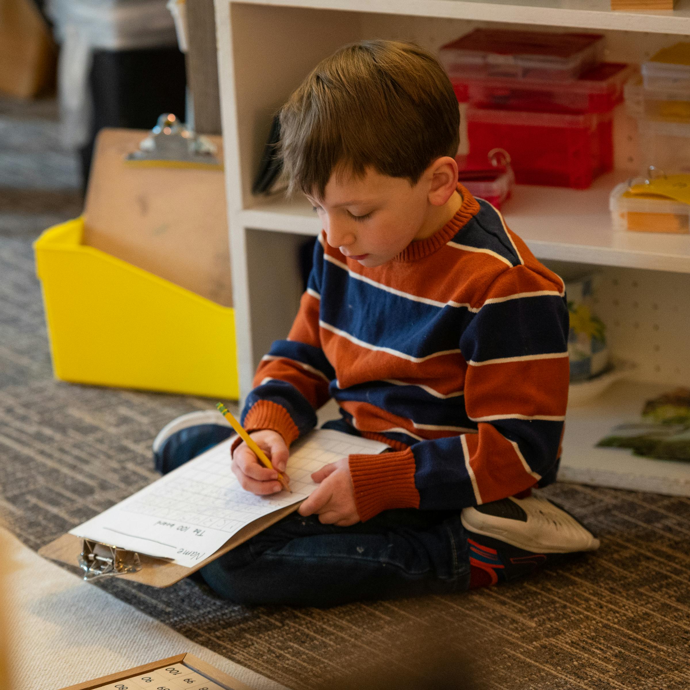 Child sitting on floor writing on a clipboard