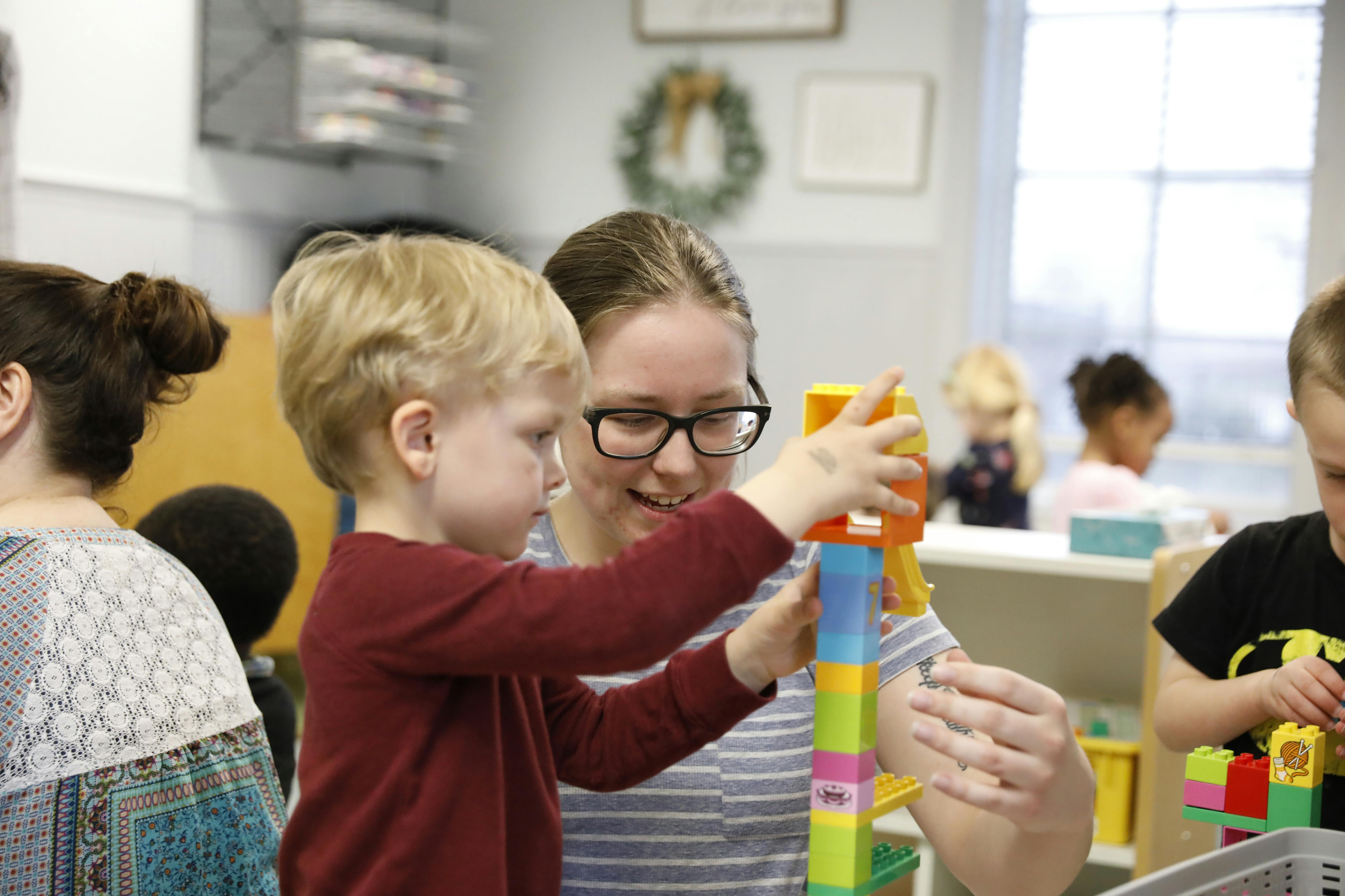 Adult and child building with colorful blocks in a classroom