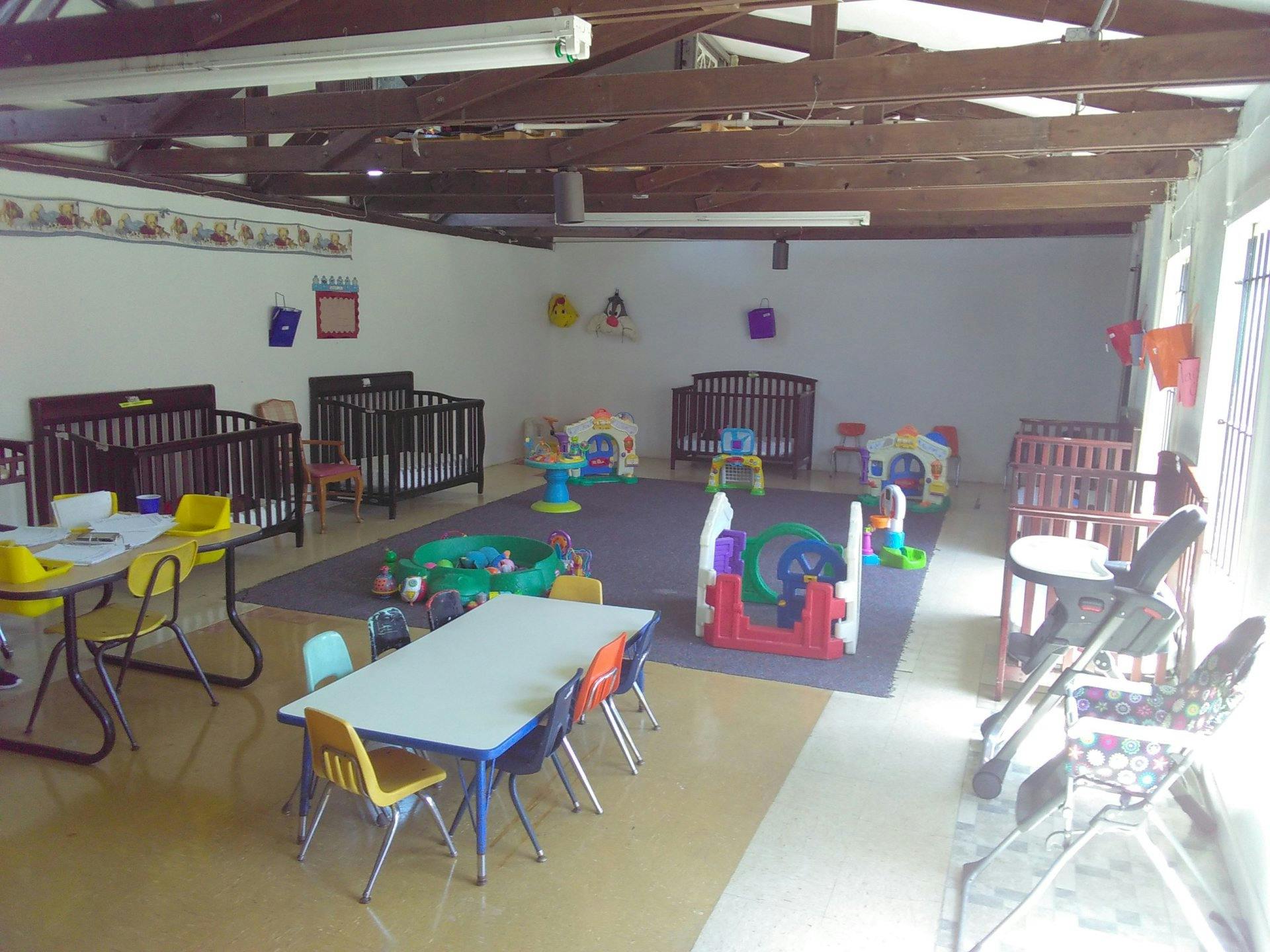 Daycare room with cribs, tables, chairs, and play mats with a padded floor area