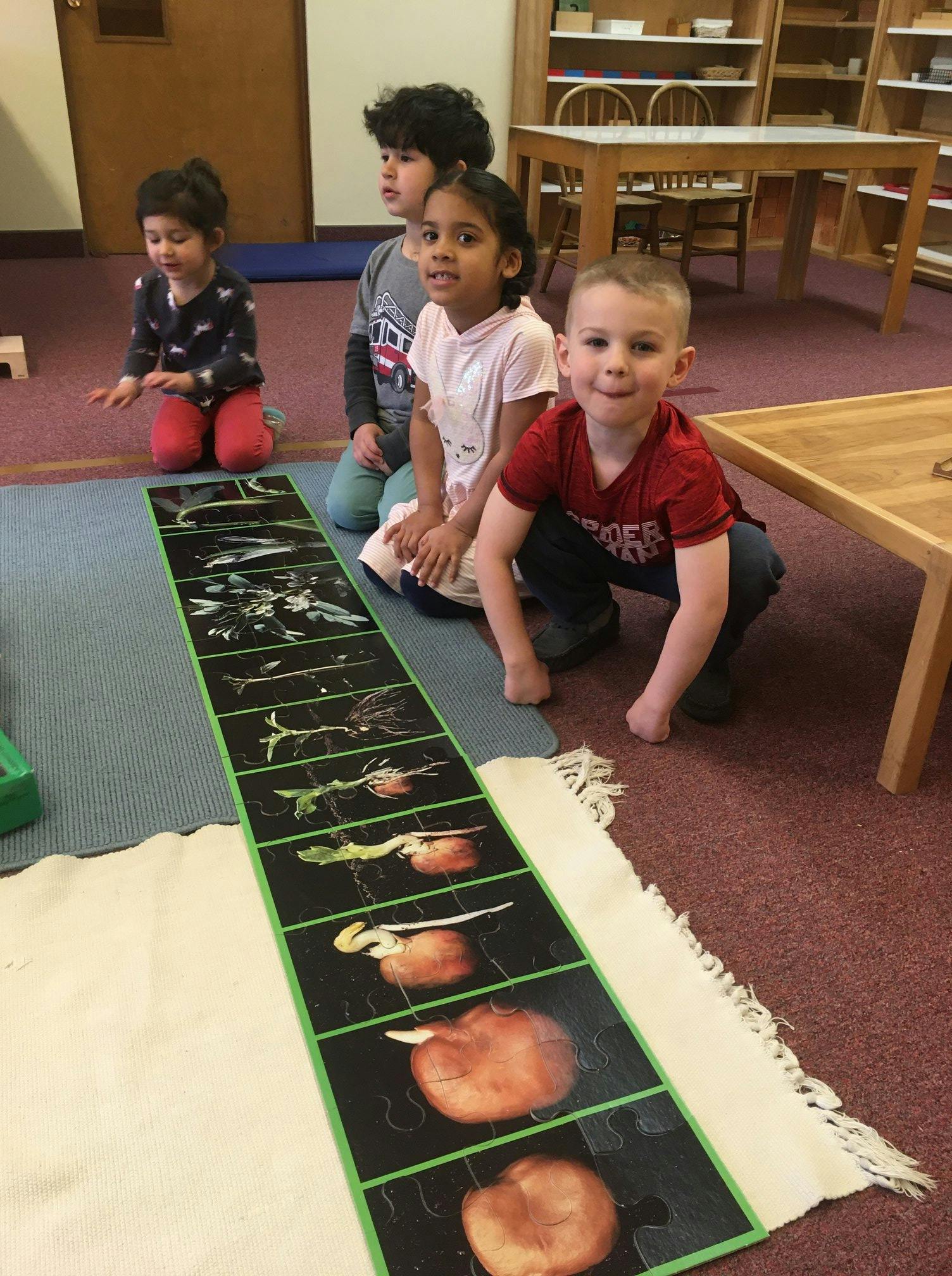 Four children kneeling around a long mat with images of plant growth stages