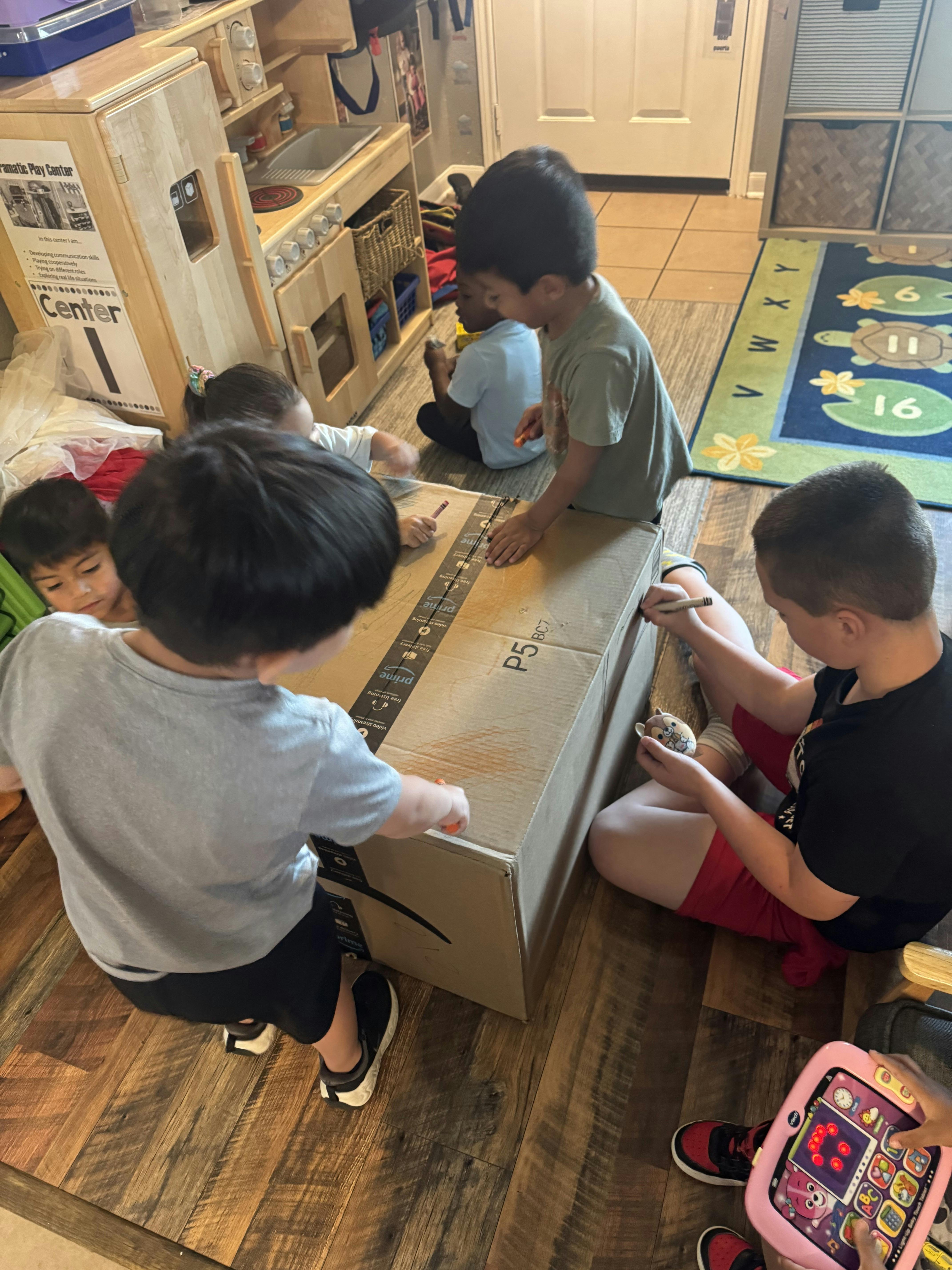Group of children drawing with crayons on a large cardboard box