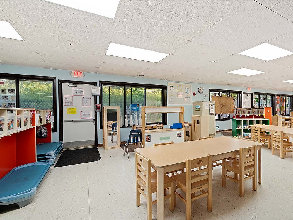 Empty classroom with small tables, chairs, and play equipment