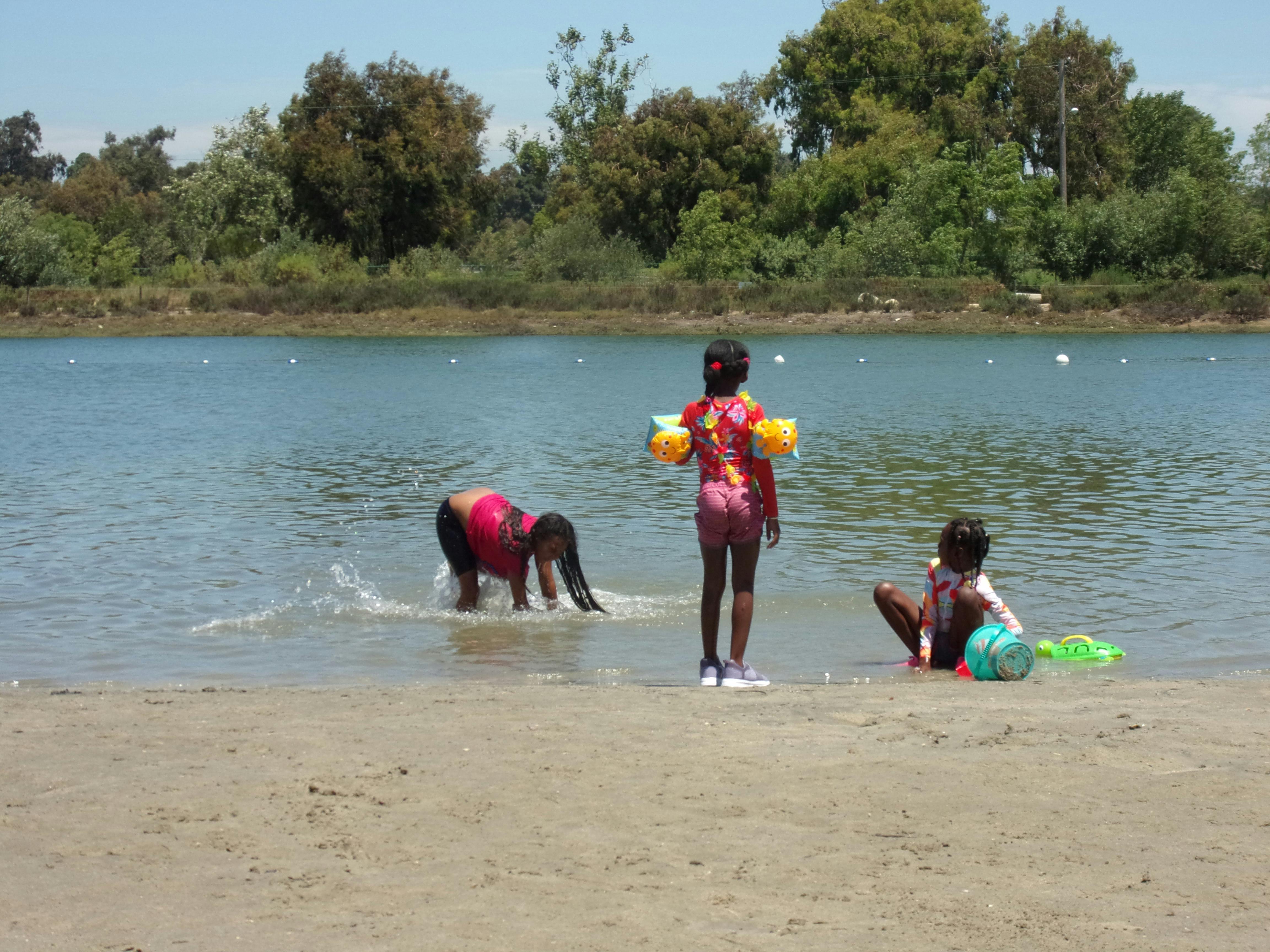 Three children playing in the shallow water at a lake's edge