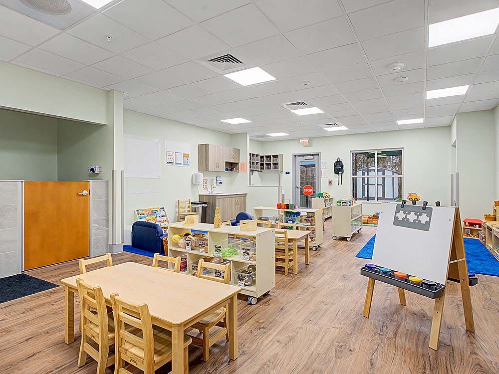 Empty classroom with small wooden tables and chairs, and a white easel