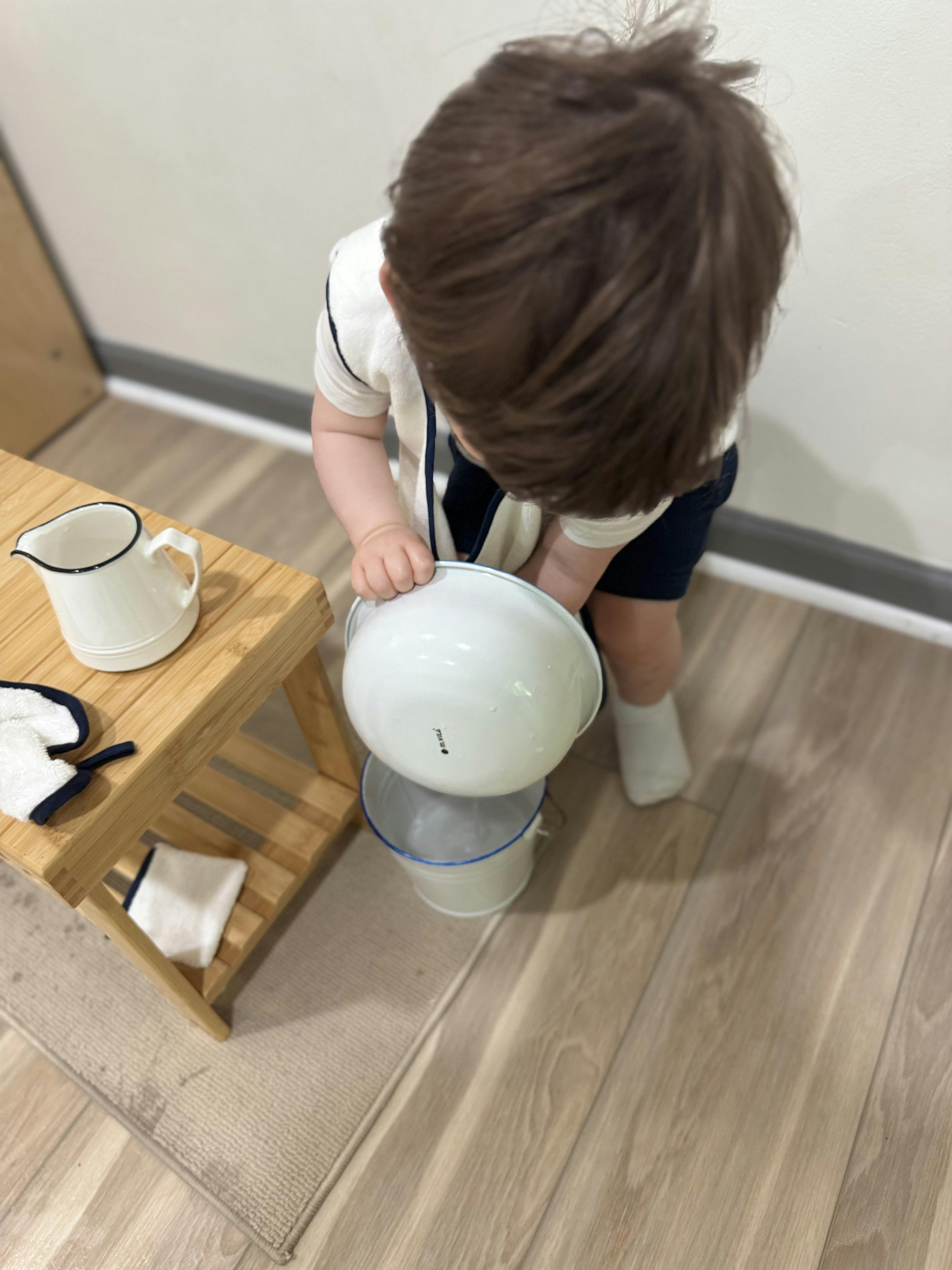 Child pouring water from a bowl into a small bucket