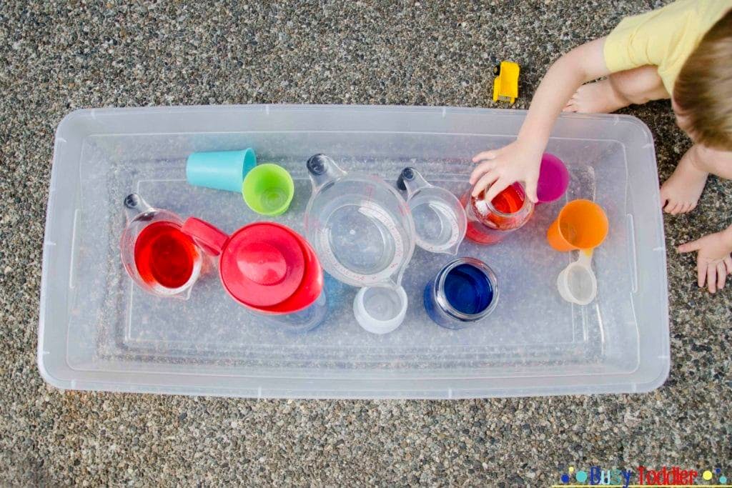 Child playing with measuring cups and water in a plastic bin