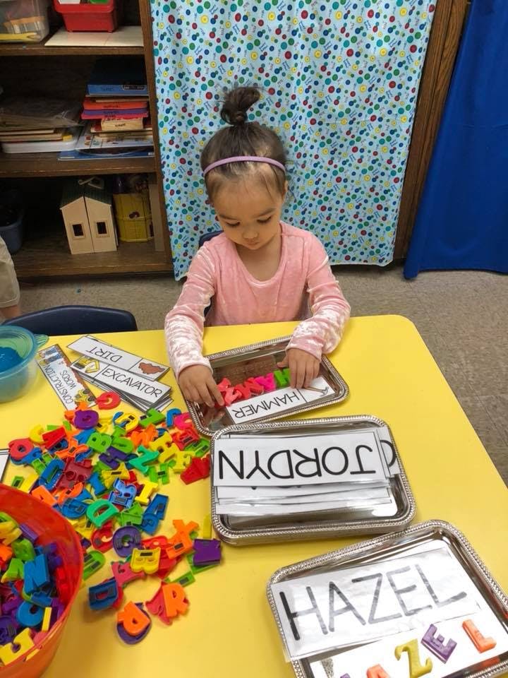 Child playing with colorful letter magnets on a yellow table