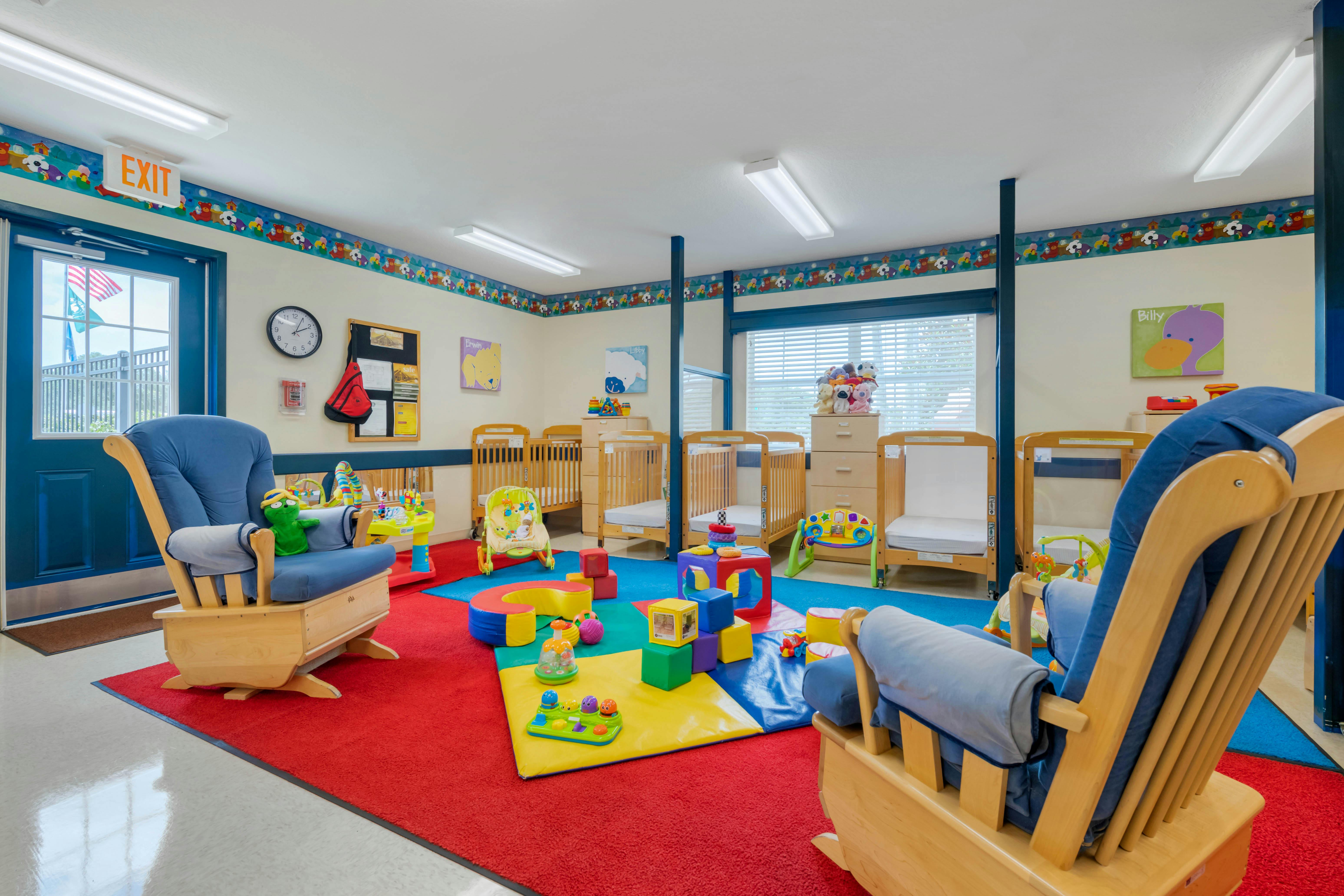 A childcare room with cribs, play mats, toys, and two rocking chairs