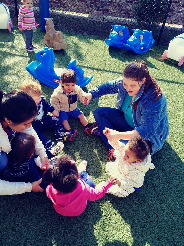 Adults and children sitting in a circle on artificial grass