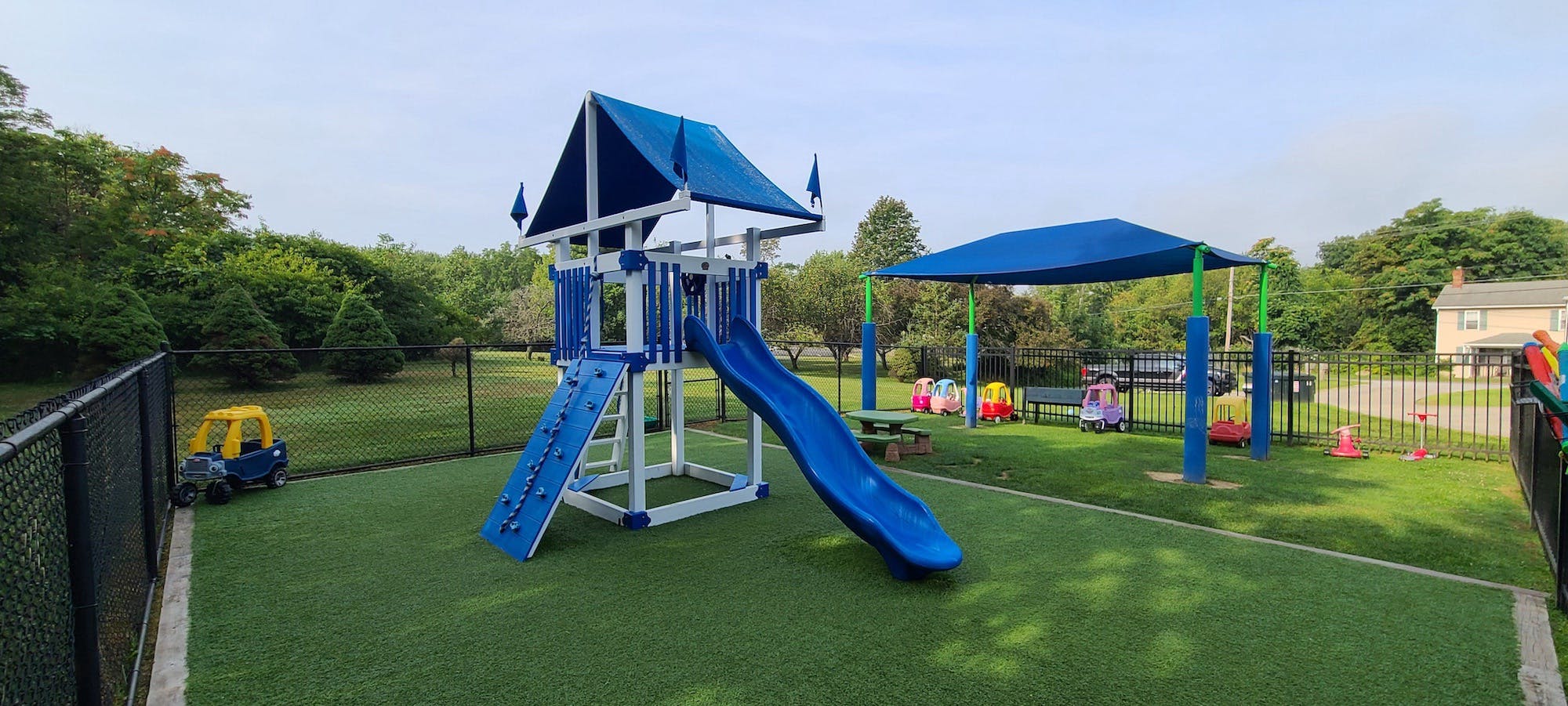 A fenced playground with blue play structure, slide, and toy cars