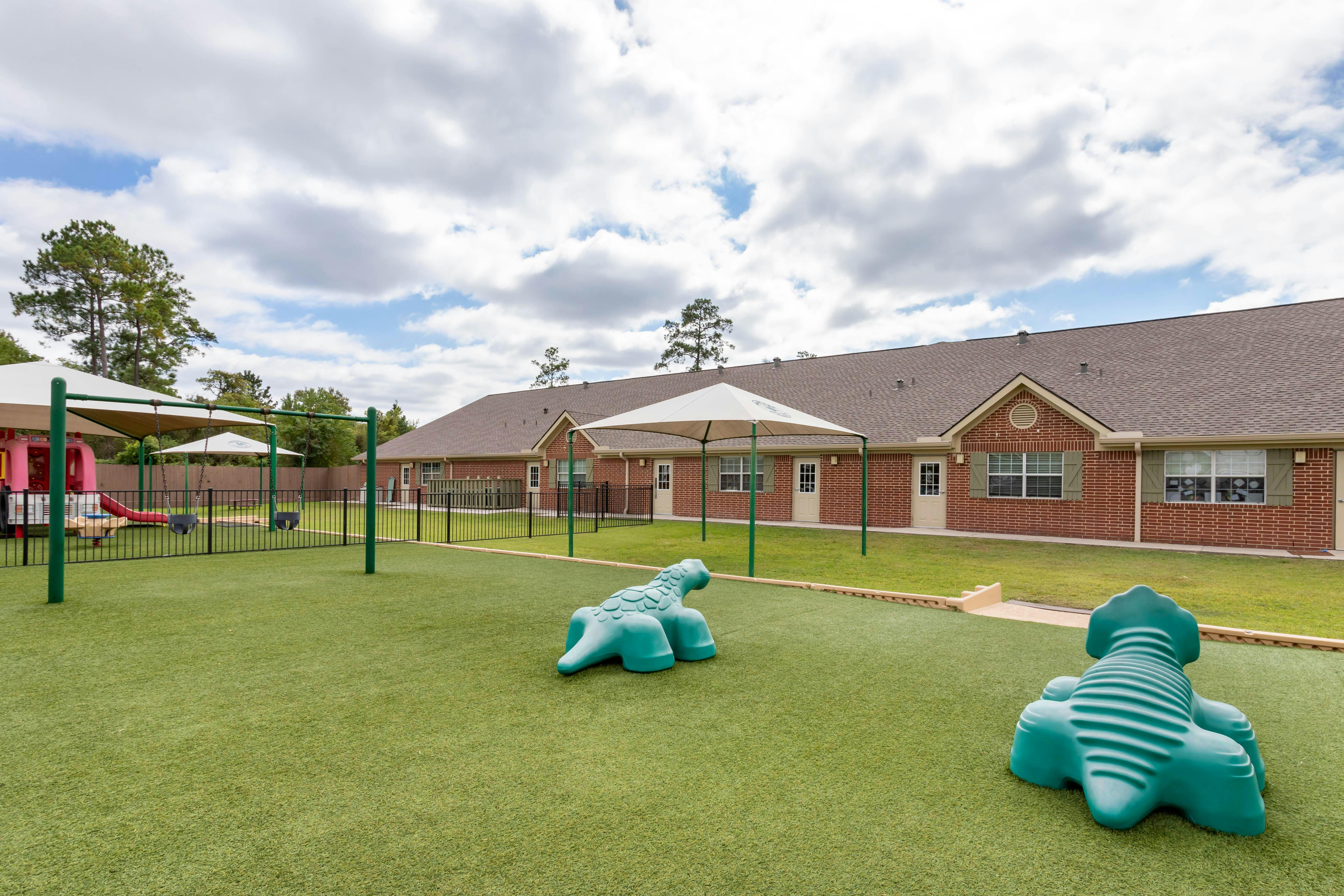An outdoor playground with swings, a red slide, and two green animal spring riders