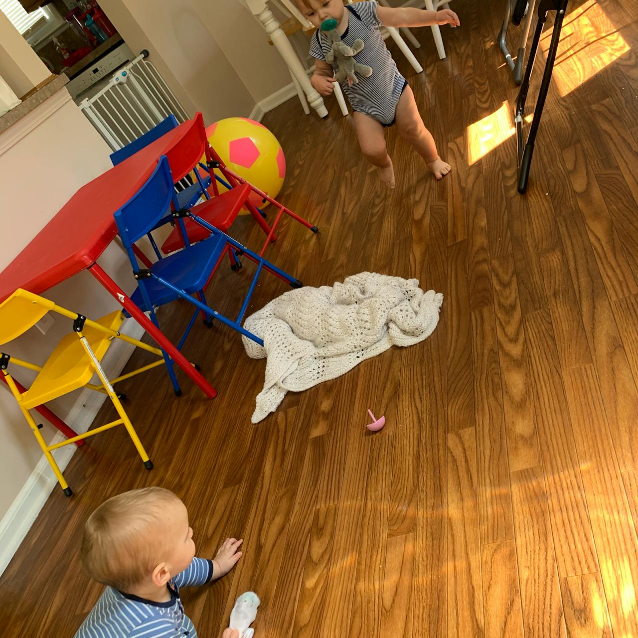 Two children on a wooden floor, one crawling and one standing