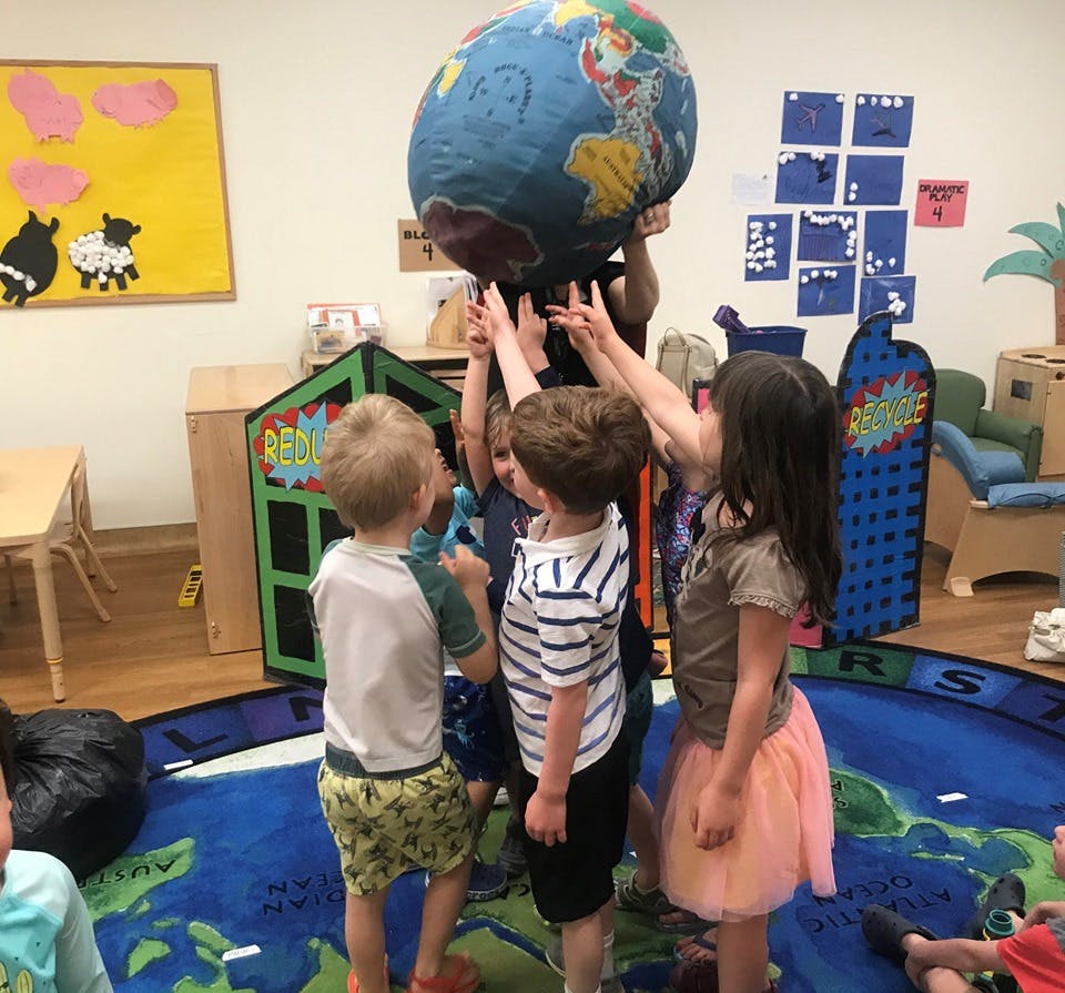 Children in a classroom reaching up to hold a large globe
