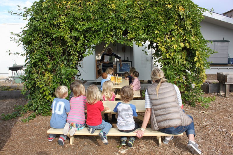 Adult and children sitting on a bench under a leafy archway