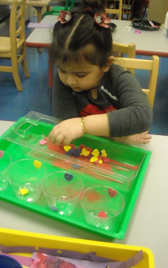 Child sorting small heart-shaped objects into cups