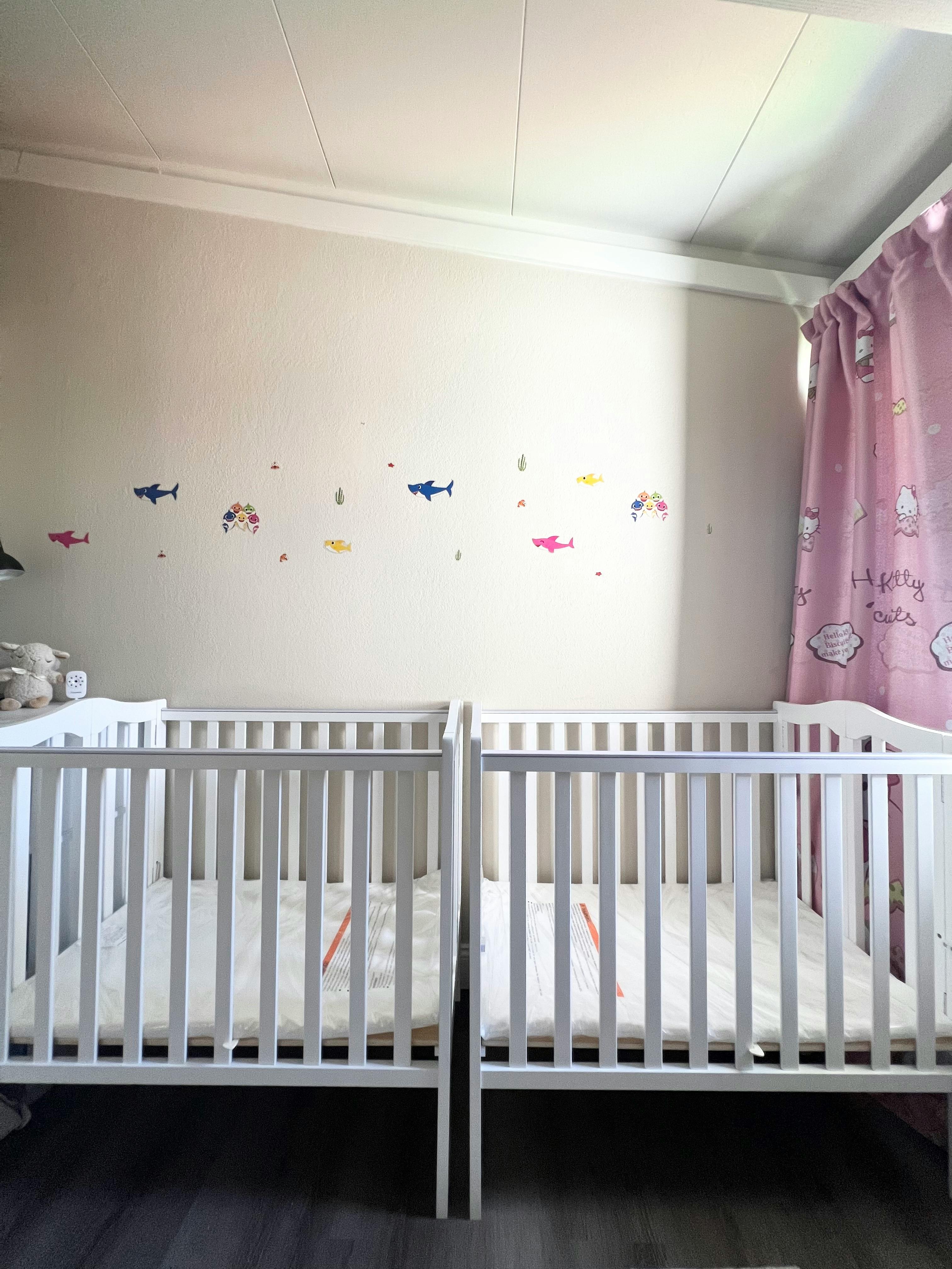 Two white cribs in a room with fish decals on the wall