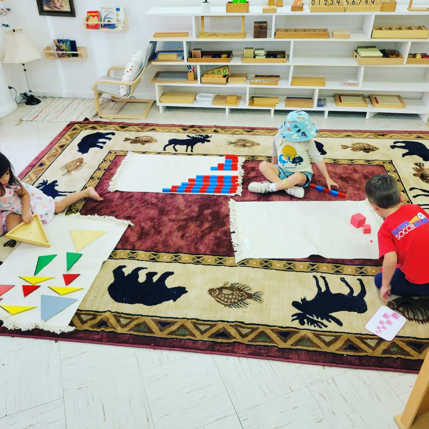 Three children playing with educational materials on a rug in a classroom