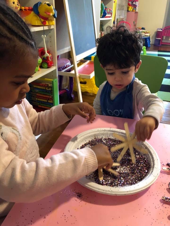Two children playing with glitter and craft sticks in a bowl