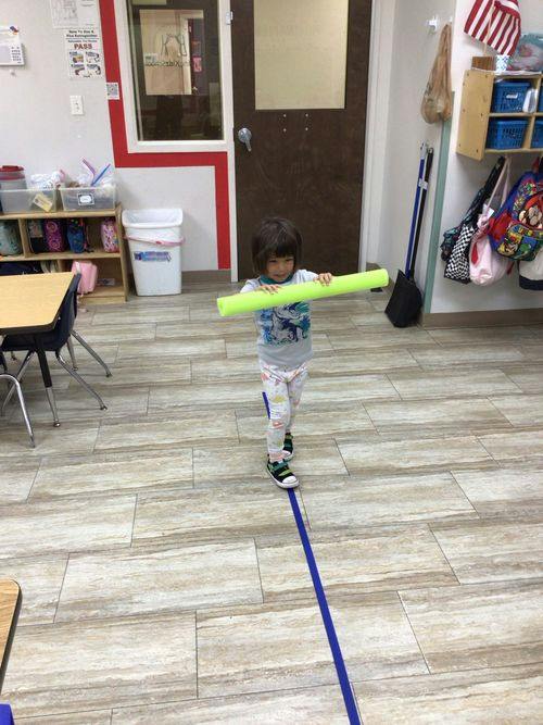 Child balancing while holding a foam pool noodle along a line on the floor