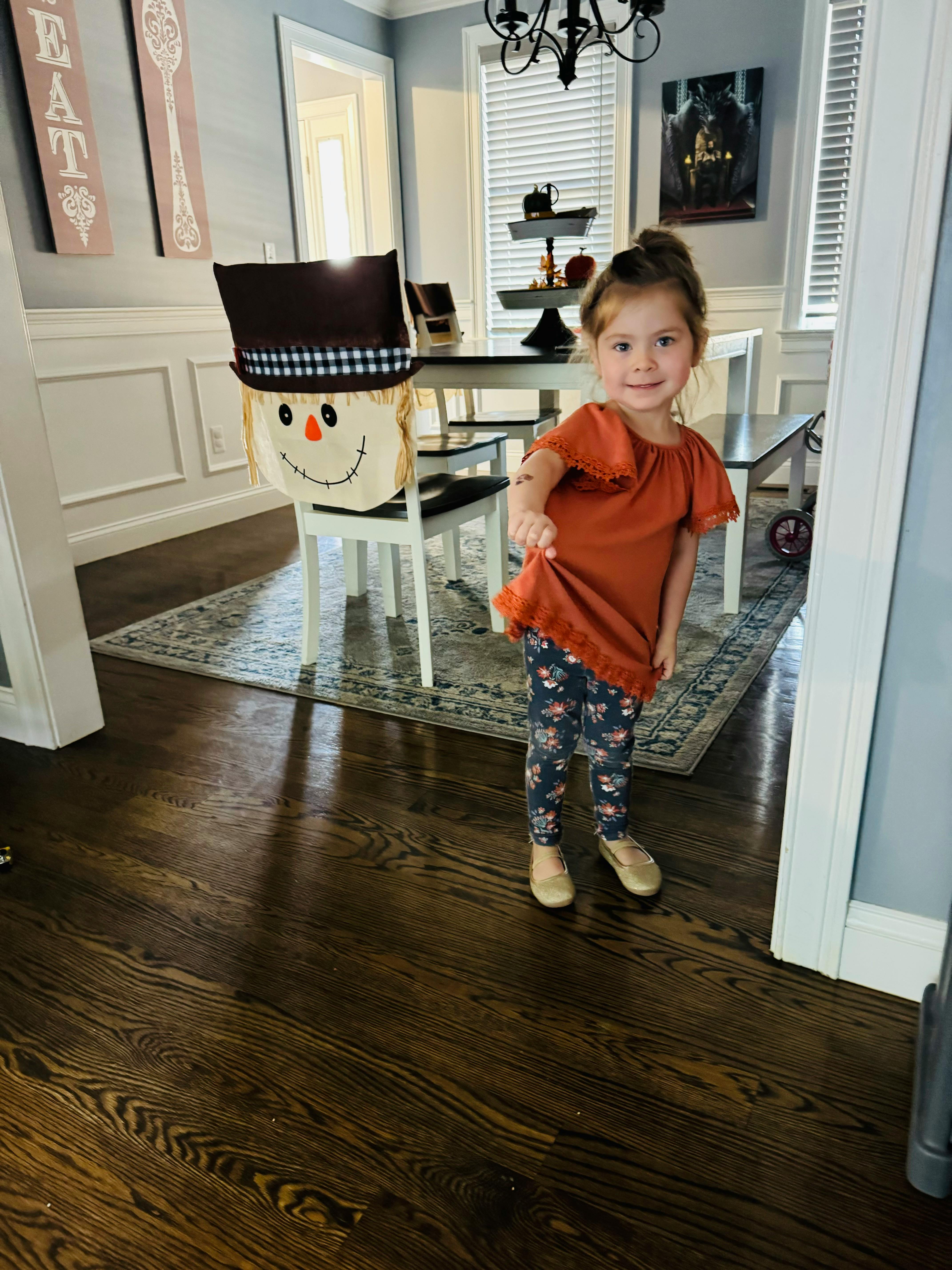 Child standing in a room with a scarecrow chair cover