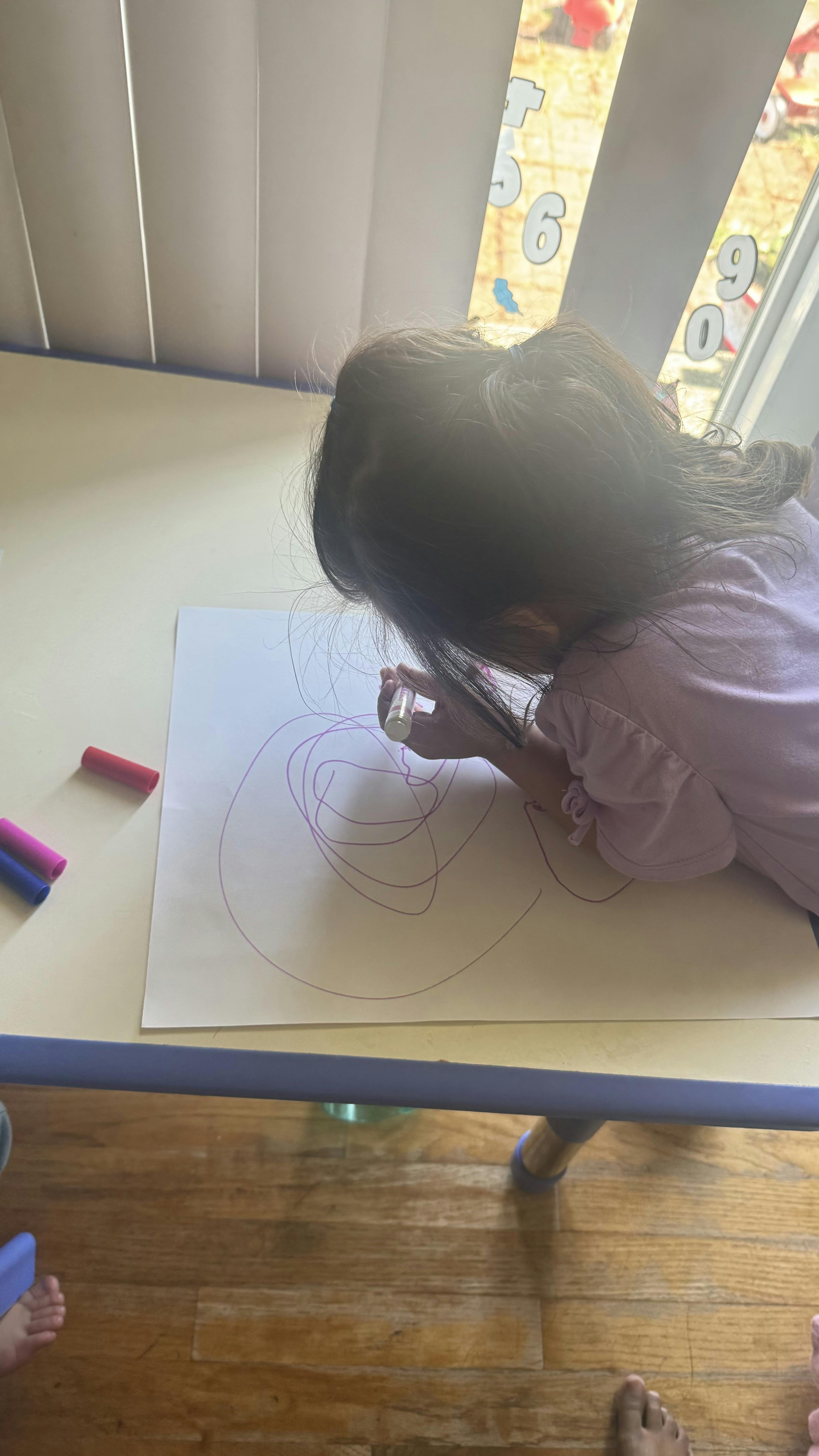 Child drawing on paper with a purple marker