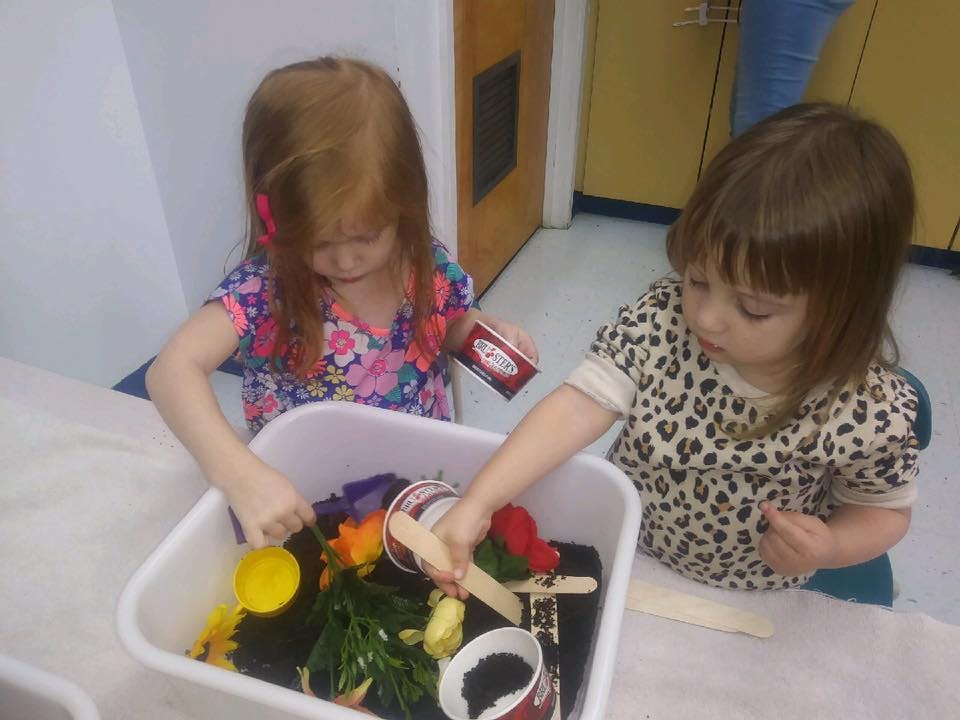 Two children playing with items in a white bin