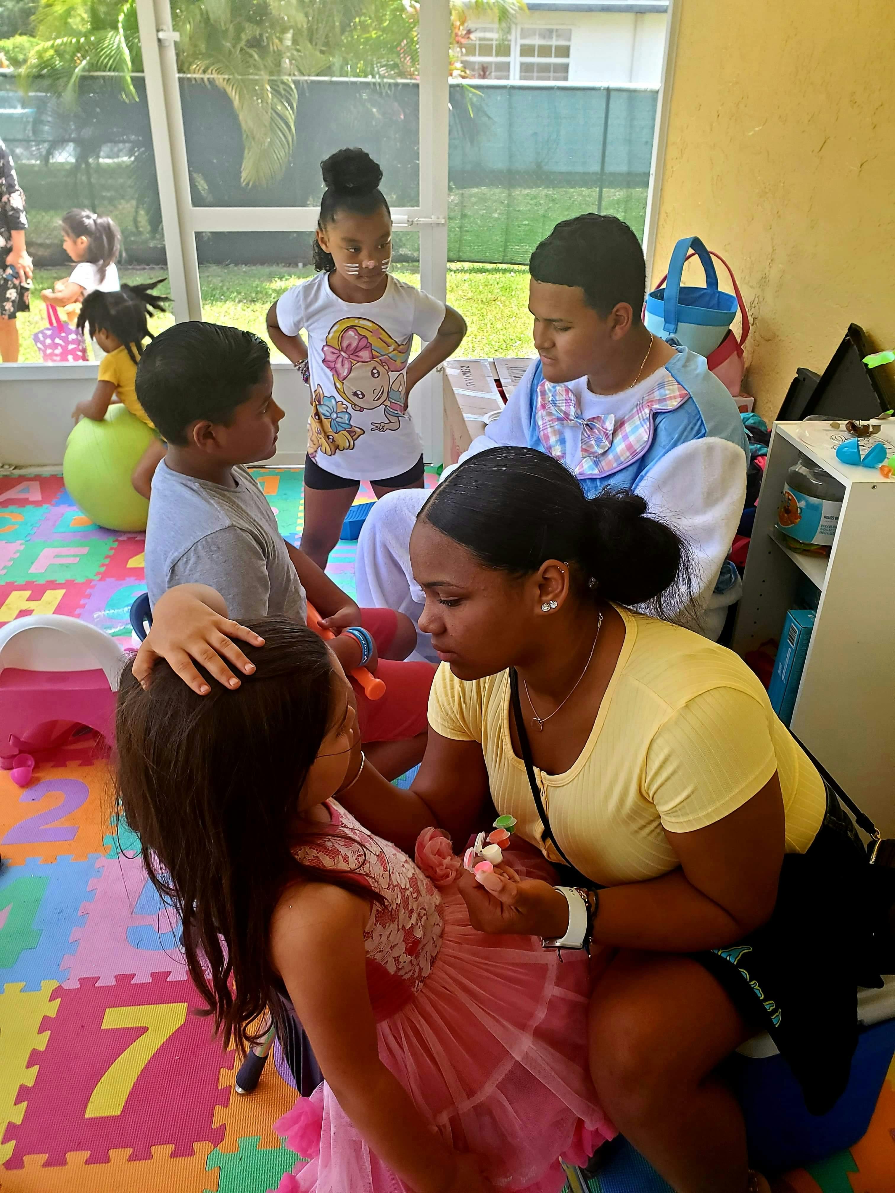 Adult applying face paint to a child, other children and adults nearby