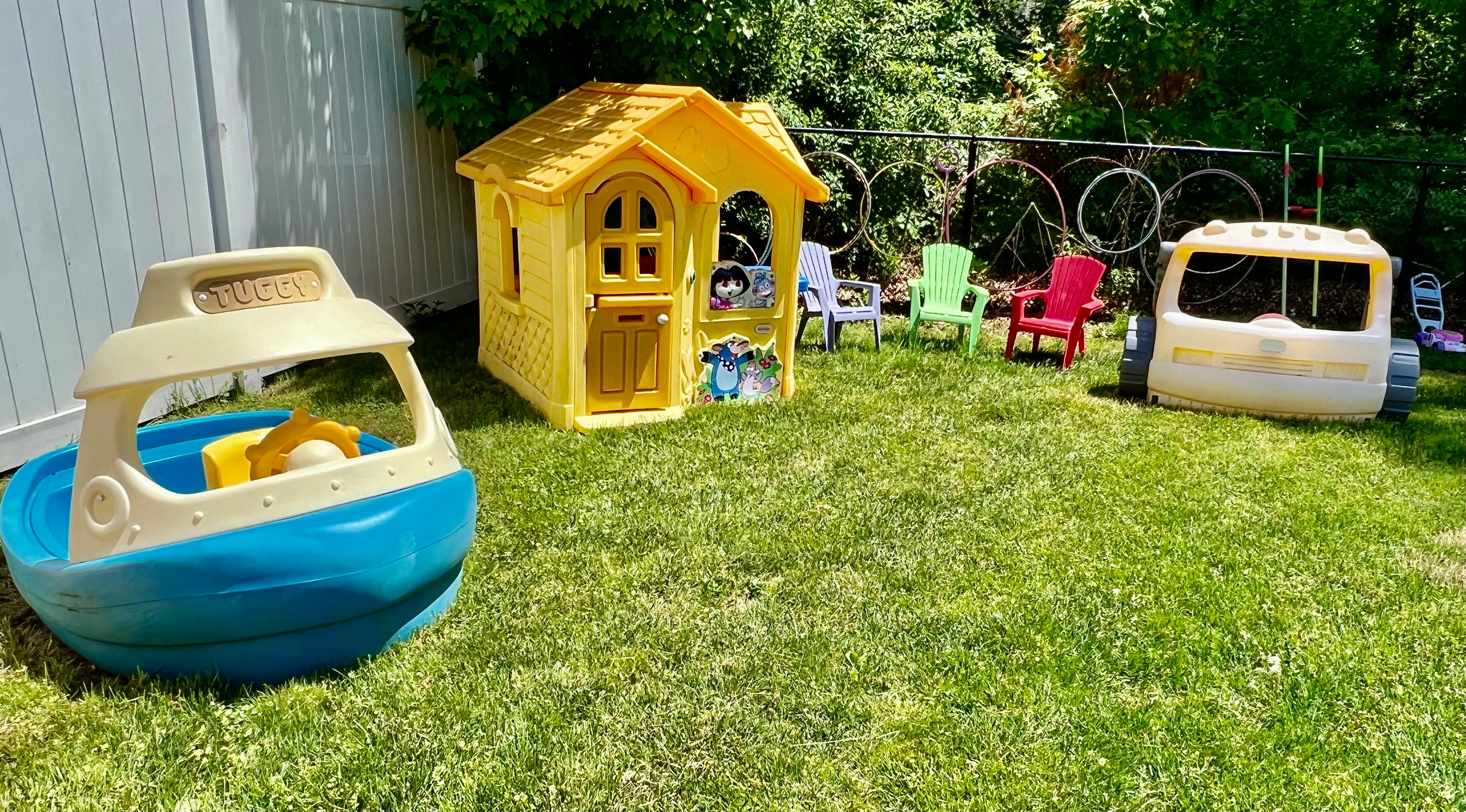 Play area with toy boat, playhouse, and toy car on grass