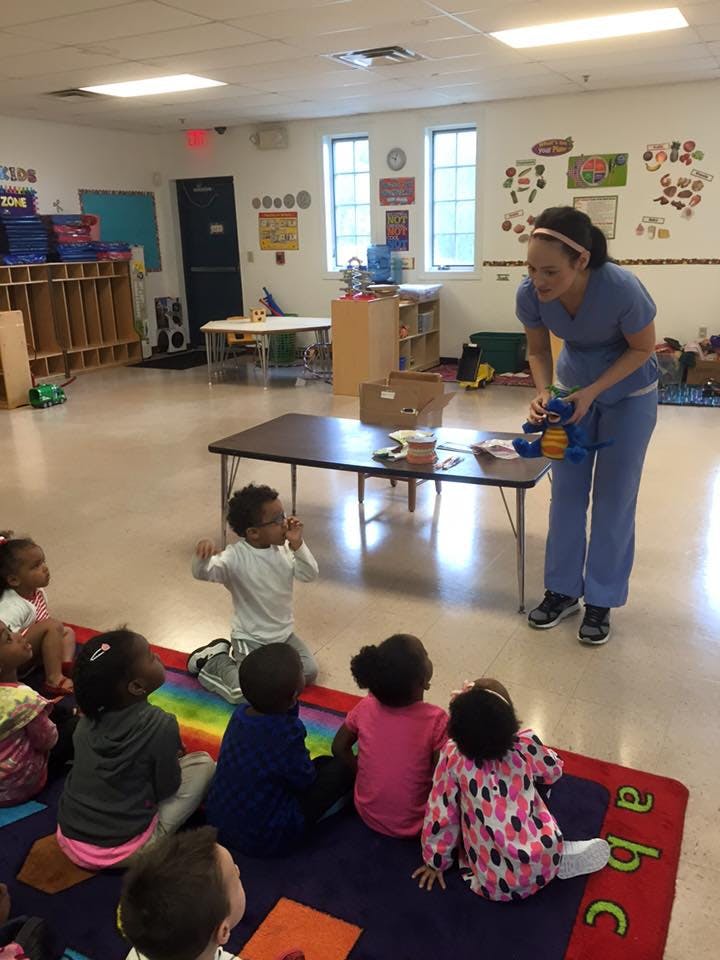 Person showing toy to children sitting on a rug in a classroom