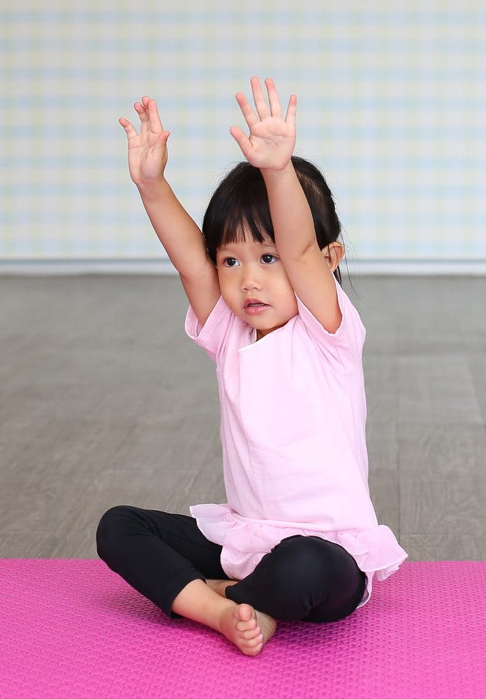 Child sitting on a pink mat with arms raised