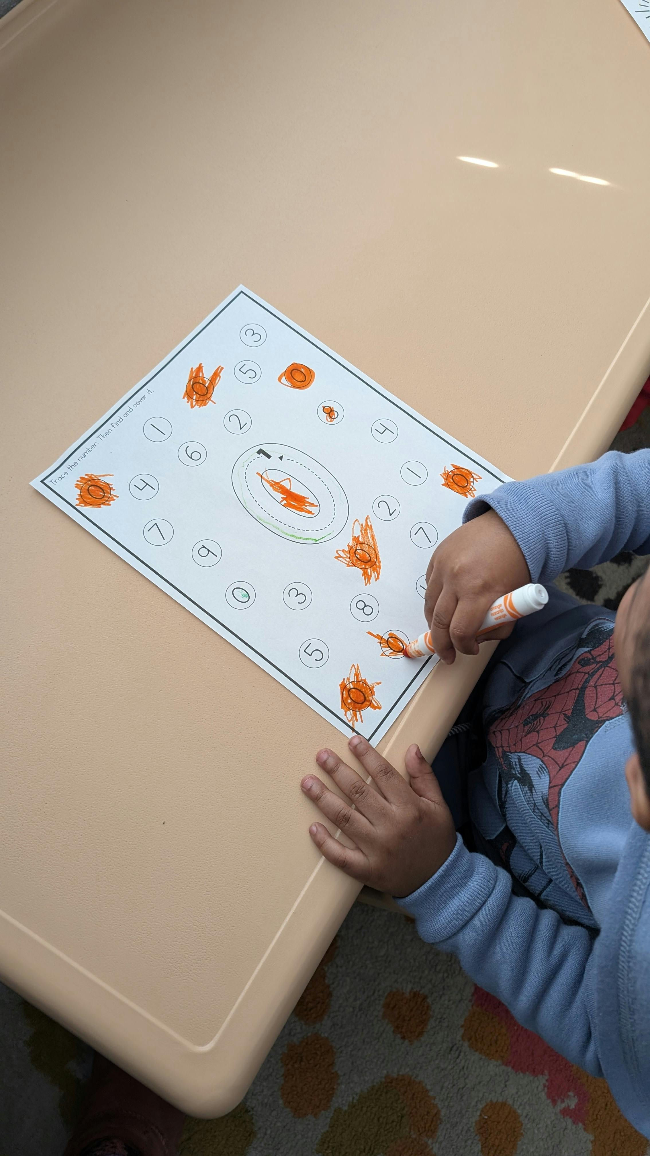 Child coloring a worksheet with numbers and shapes