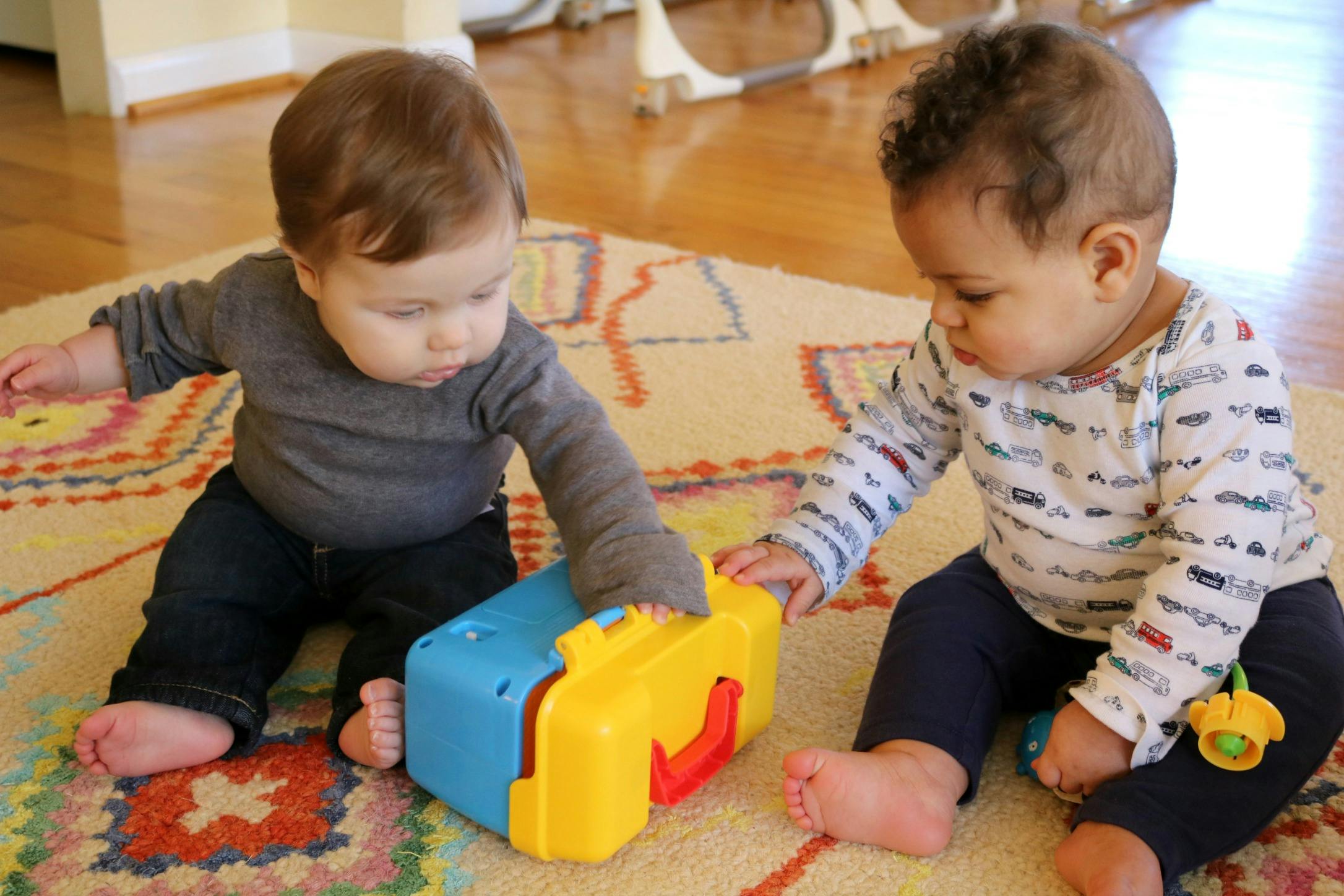 Two children sitting on a rug playing with a toy