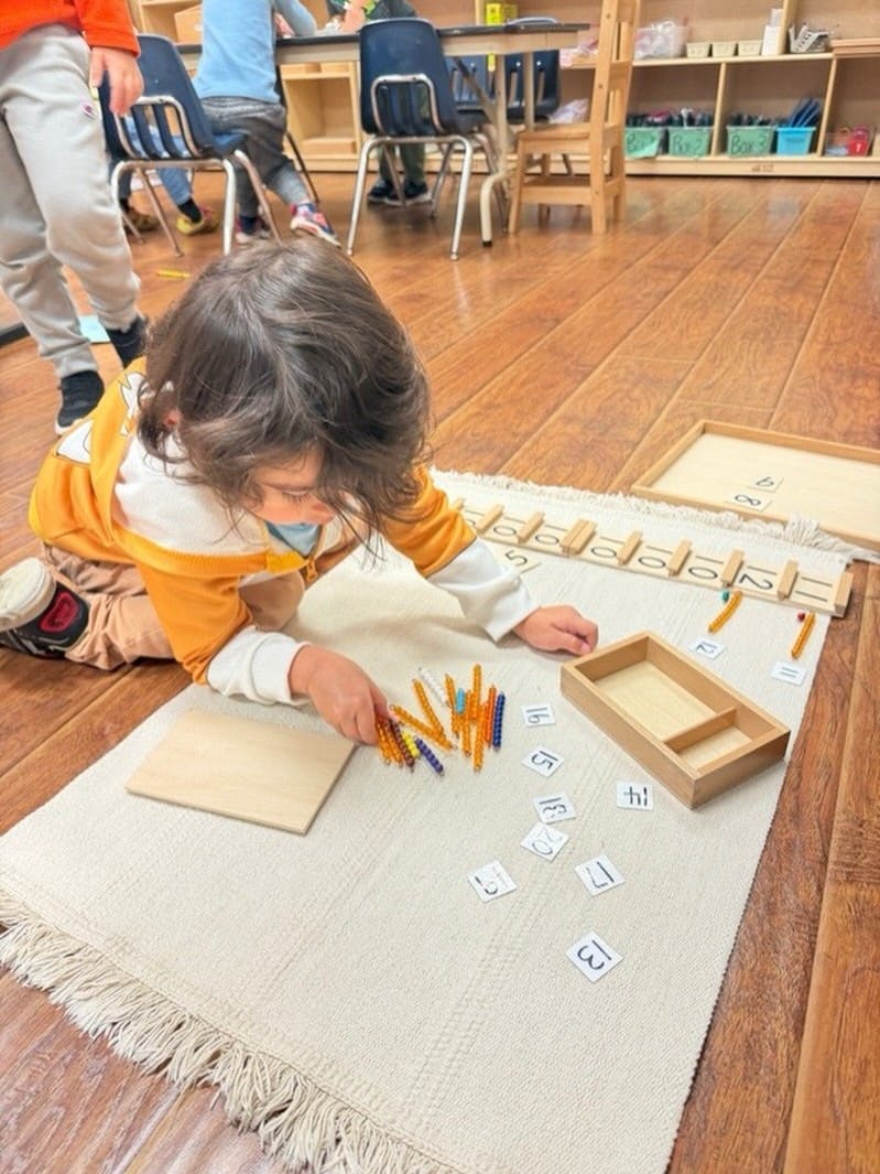 Child on floor with Montessori math beads and number cards in a classroom