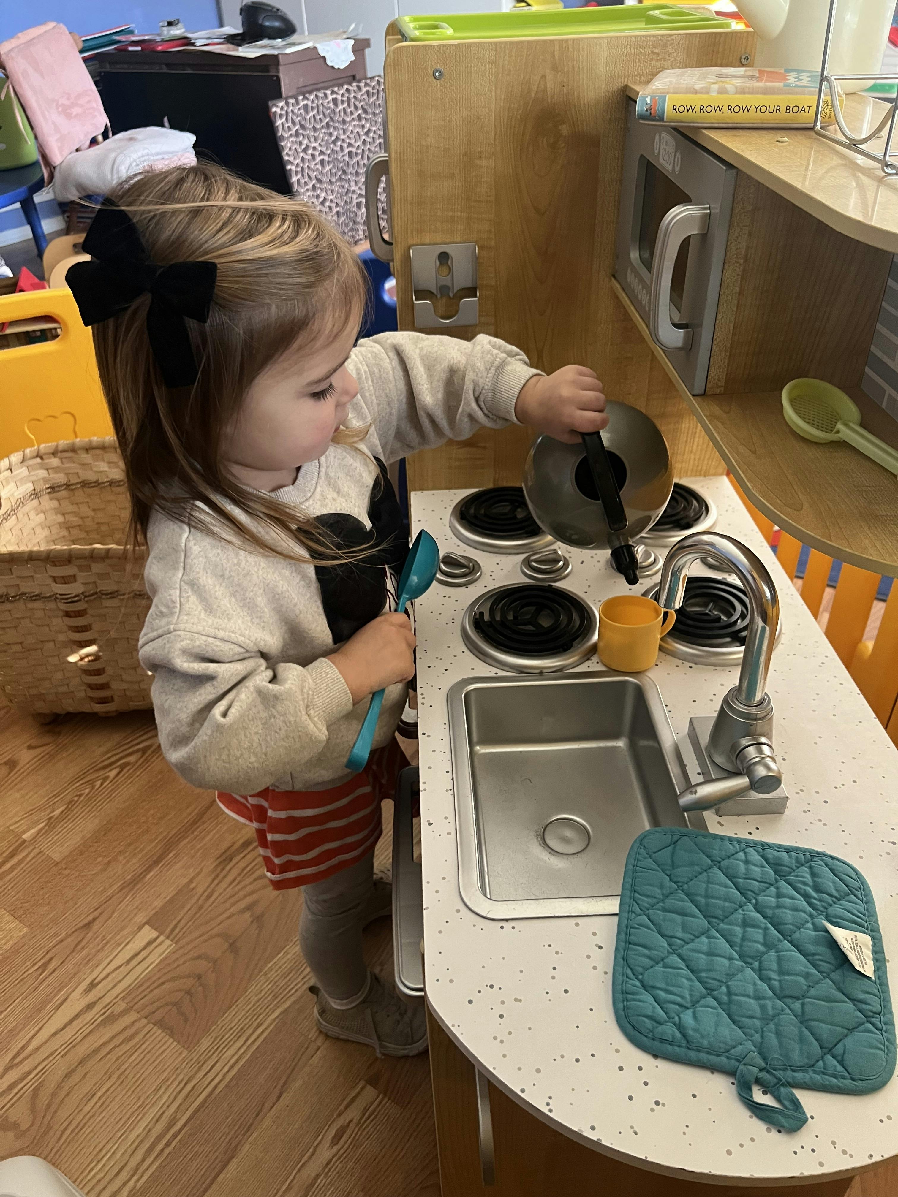 Child playing with a toy kitchen and holding a tea kettle