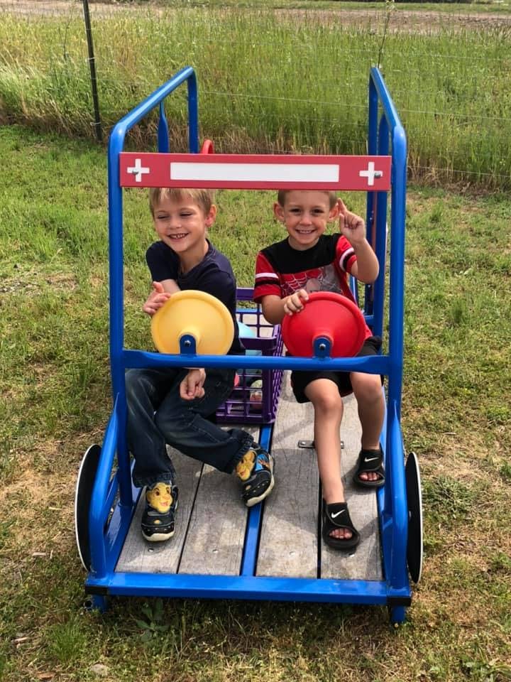 Two children sitting in a blue play vehicle with red and white accents