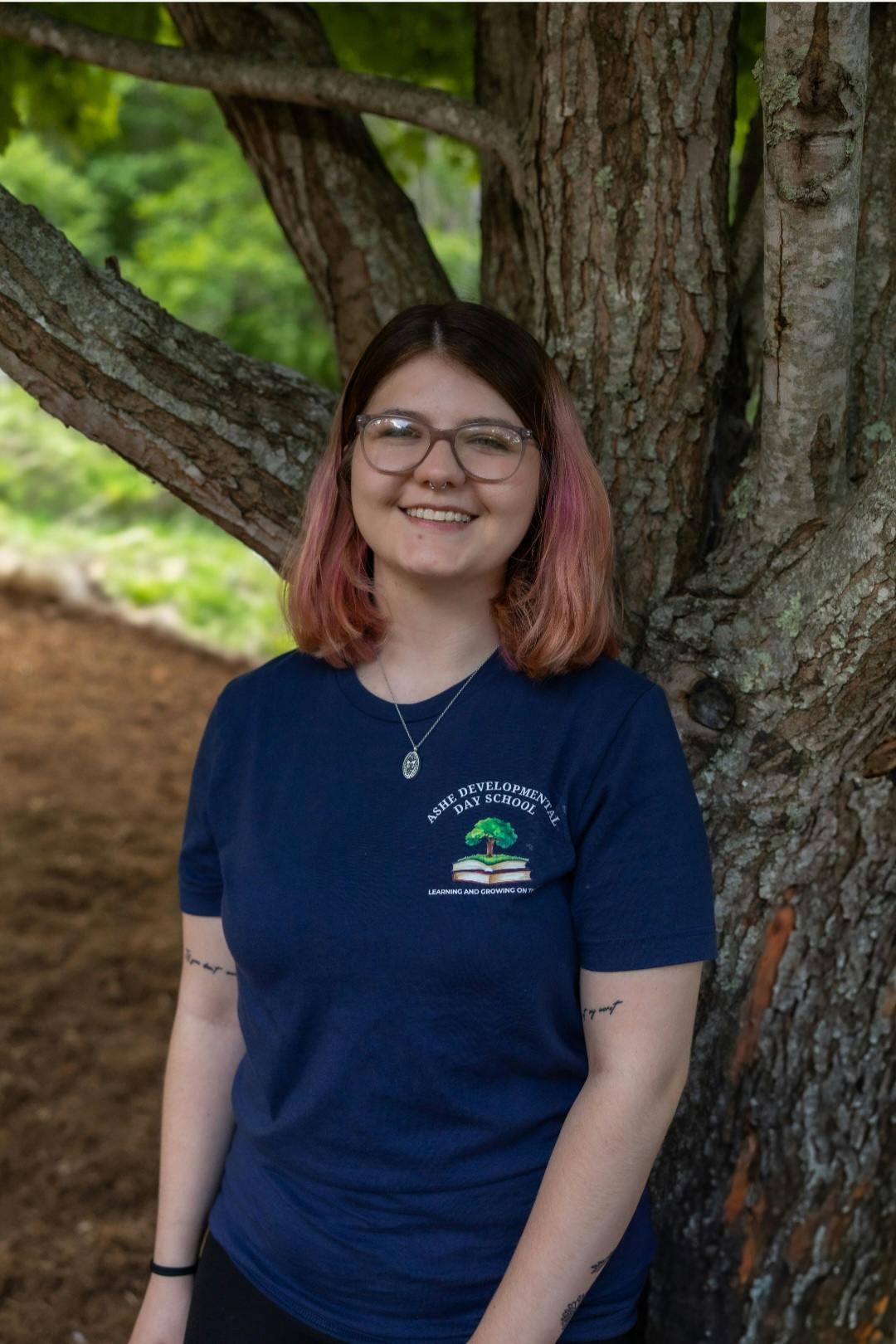 Person wearing an Ashe Developmental Day School shirt standing by a tree