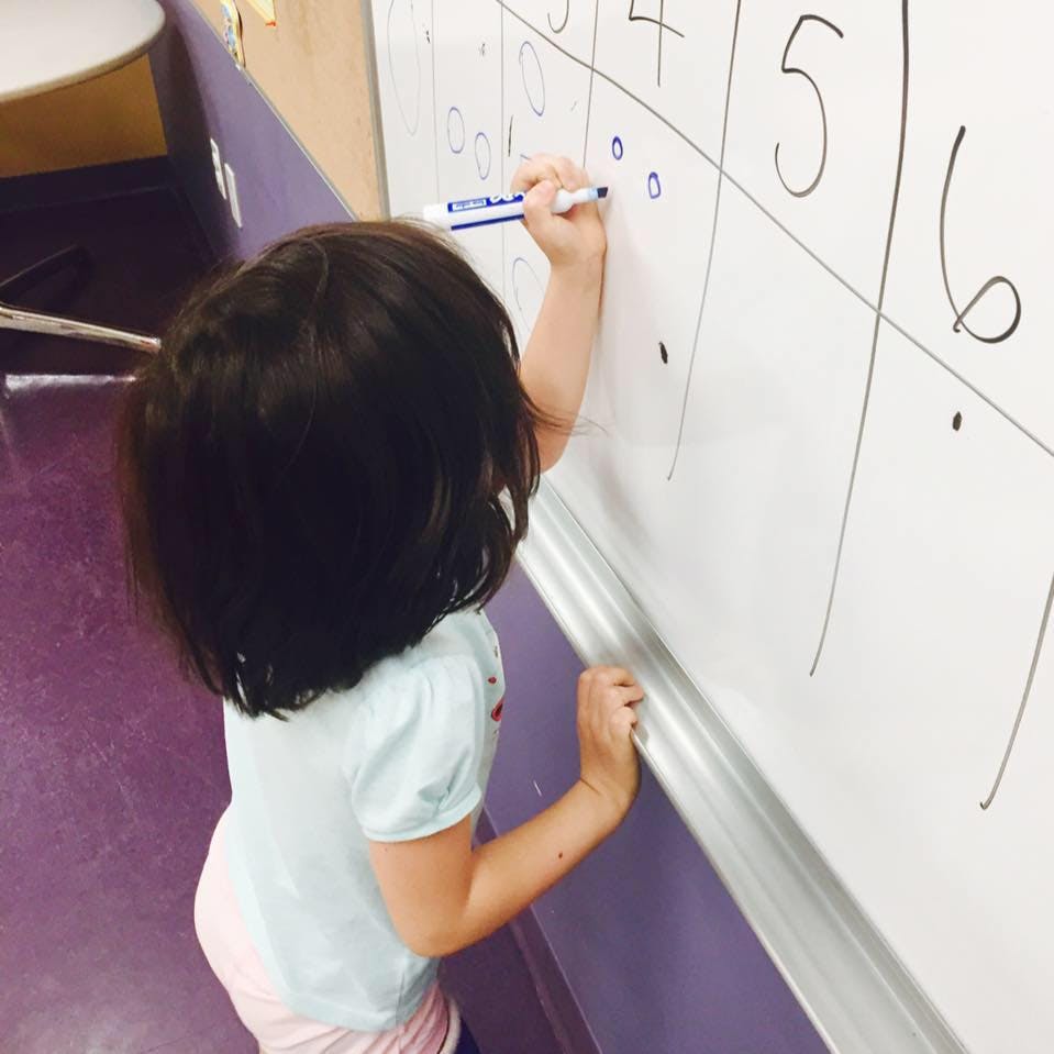 Child writing on a whiteboard in a classroom