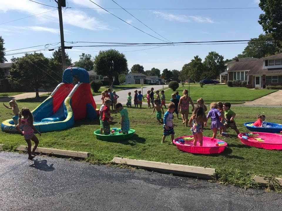 Children playing in inflatable pools and on a water slide in a yard