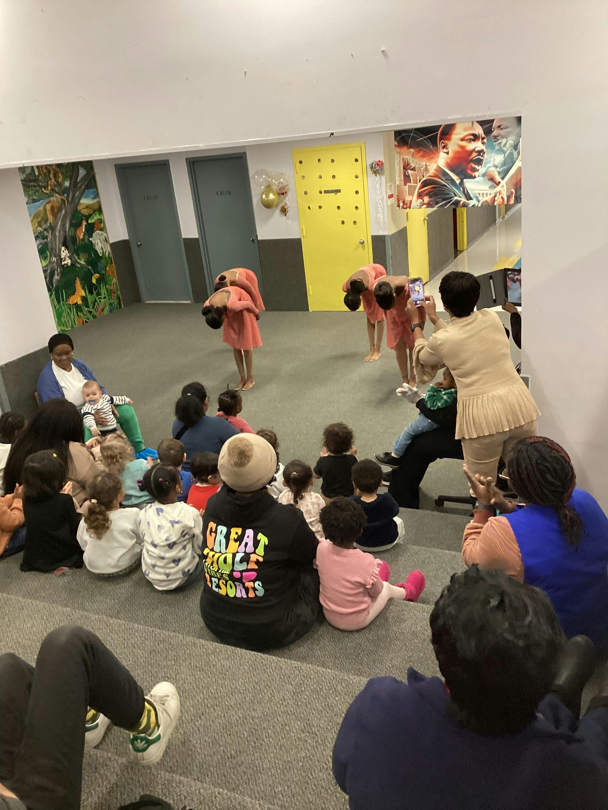 People and children gathered on the floor, some looking at a person filming