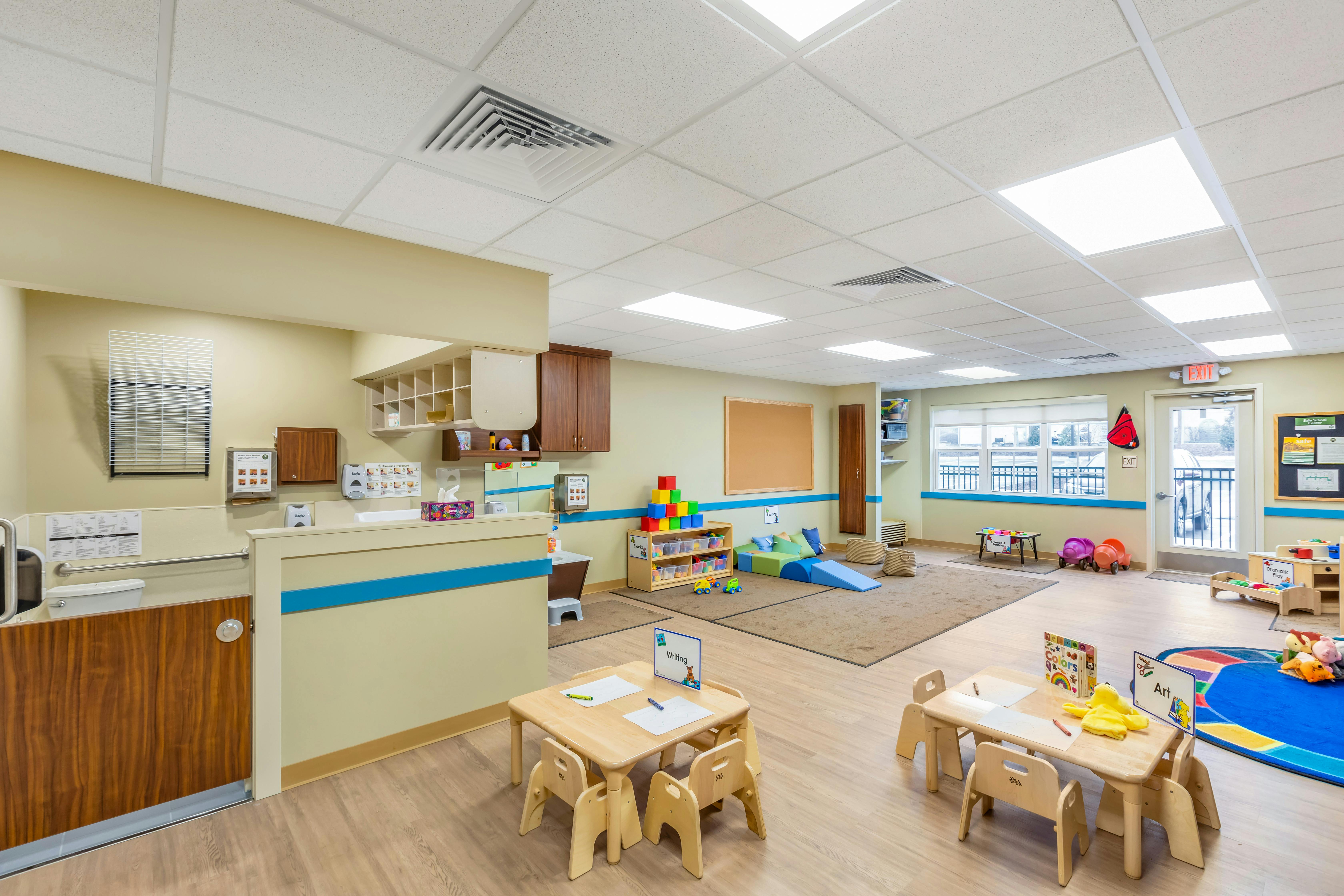 Classroom with tables and chairs for children, play area, and changing station
