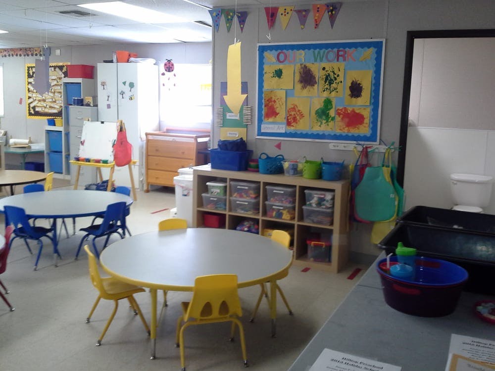 Classroom with small tables and chairs, storage shelves, and a bulletin board