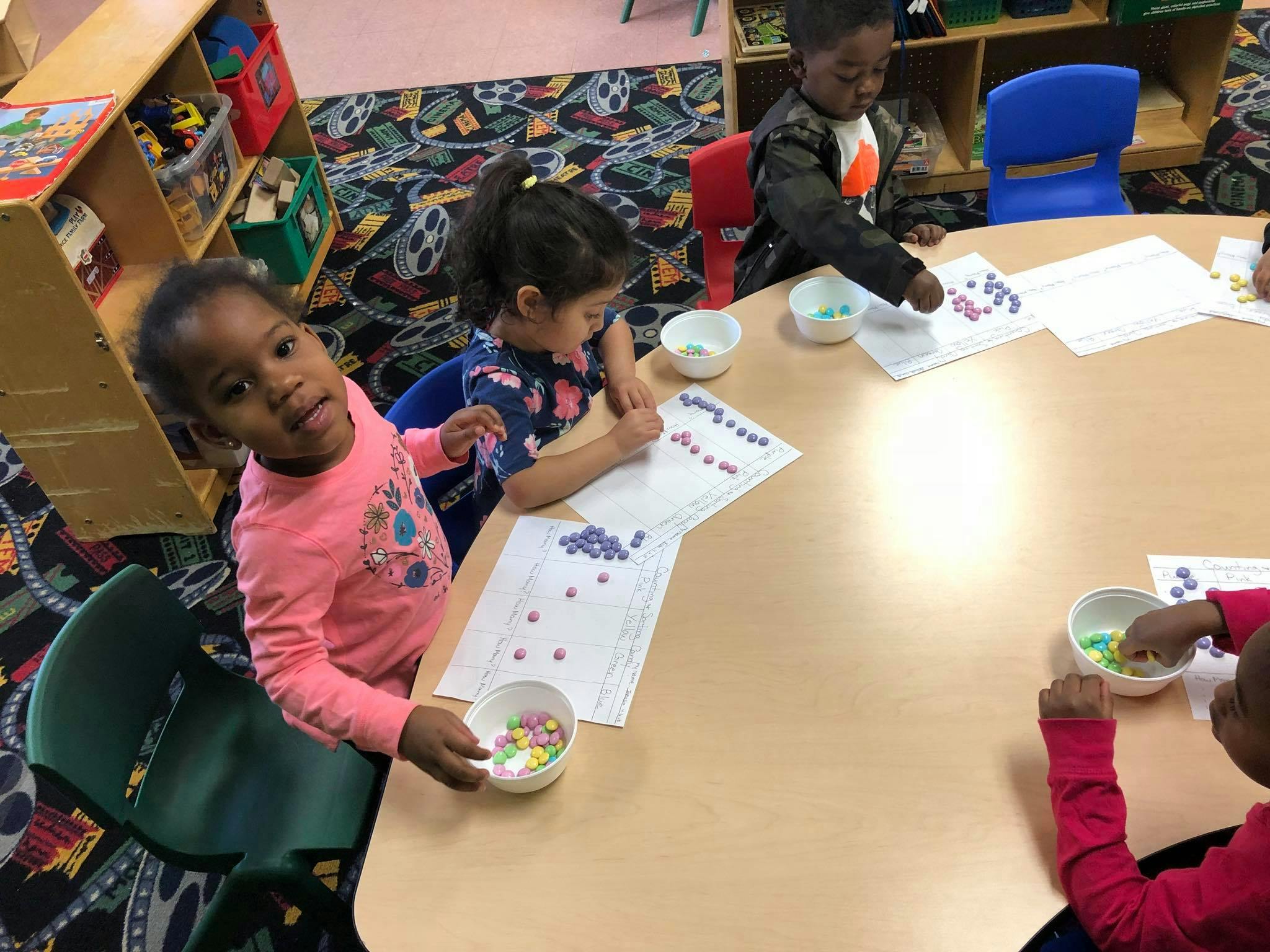 Children at a table with papers and small colorful objects