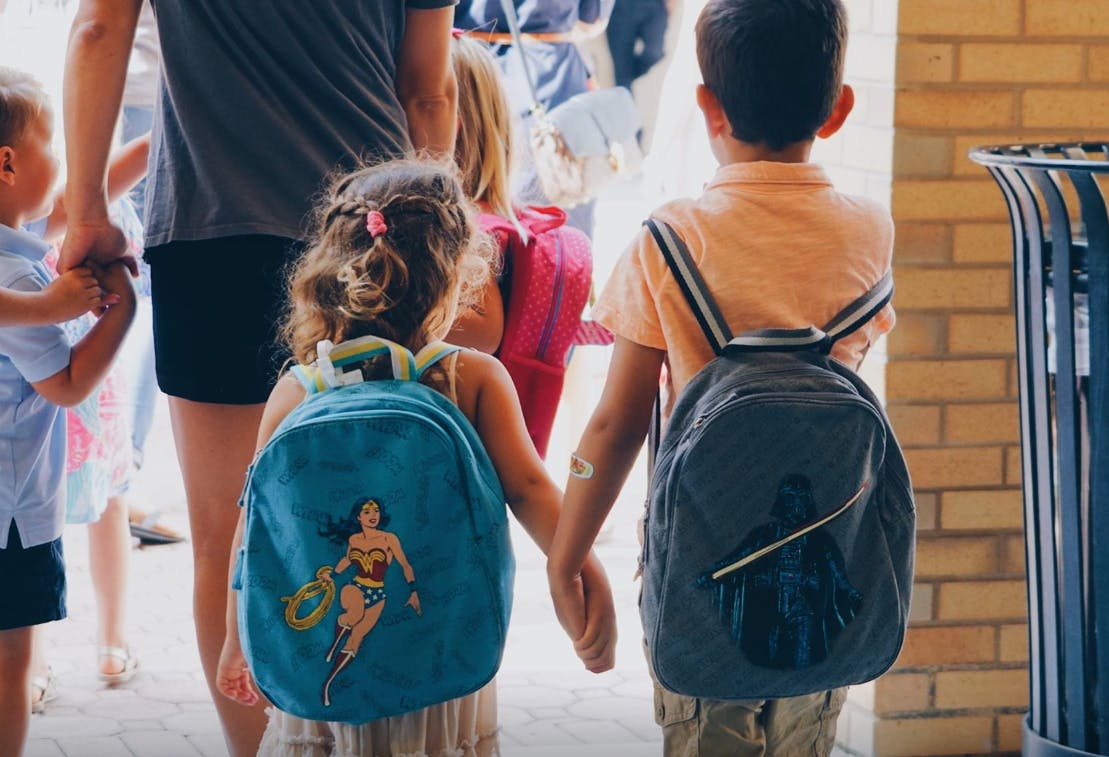 Two children with backpacks holding hands