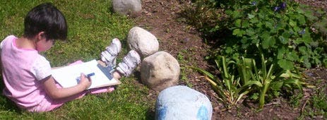 Child sitting on grass drawing on a clipboard