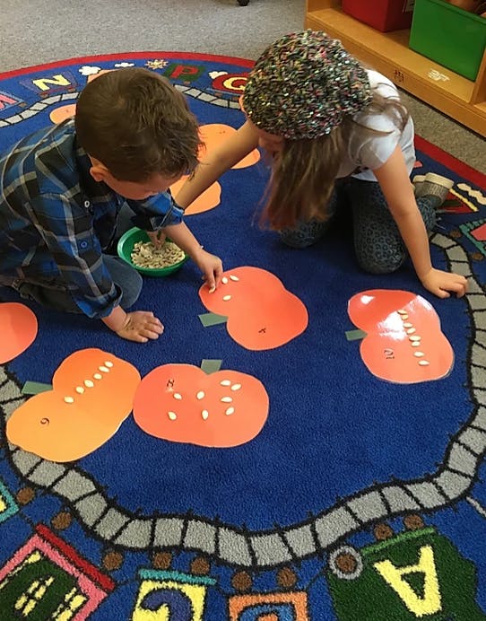 Two children on a rug placing seeds on pumpkin cutouts