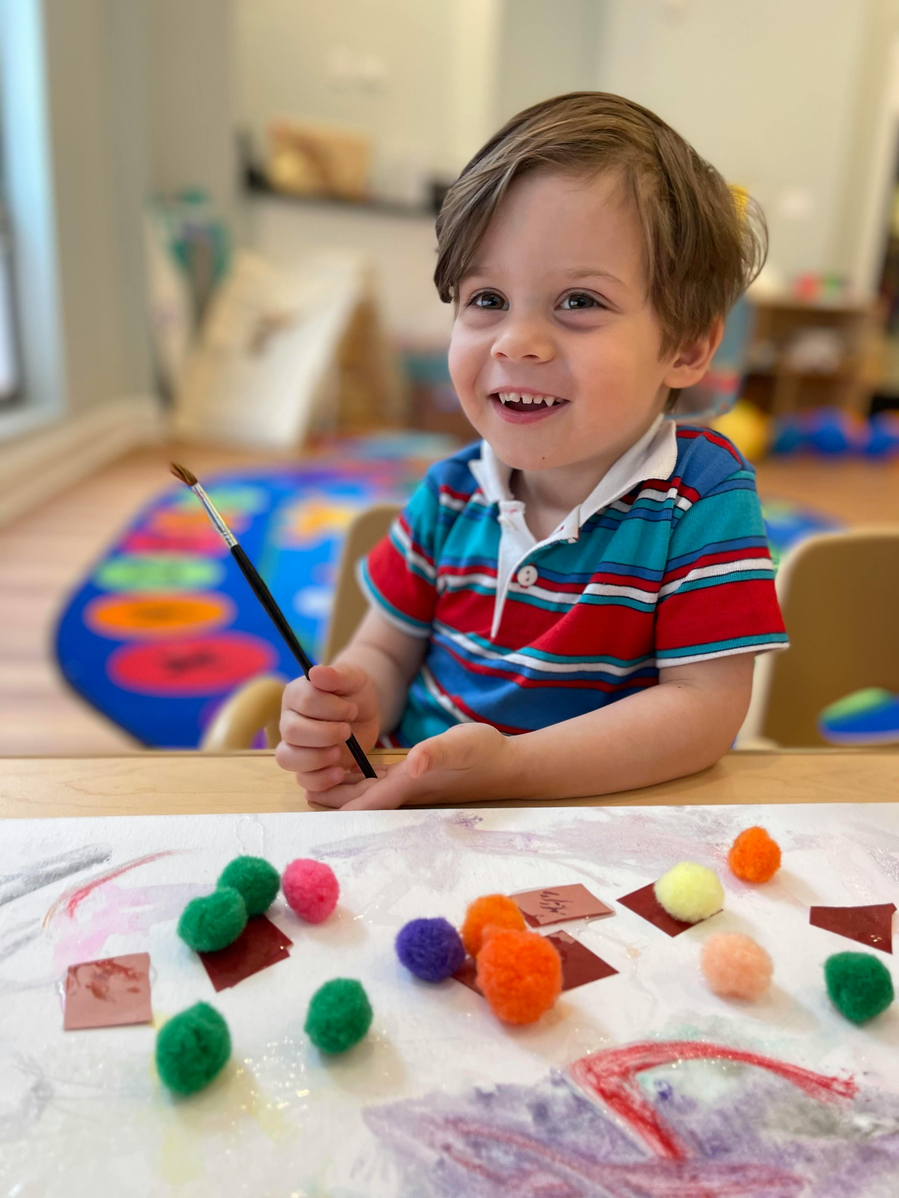 Child holding a paintbrush at a table with craft supplies